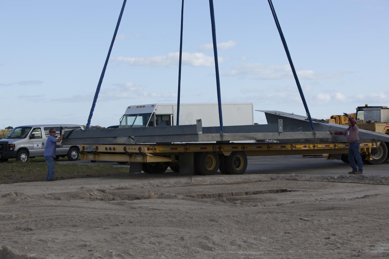 CAPE CANAVERAL, Fla. – Construction workers assist as a crane lowers a large portion of the launch pad for the Project Morpheus prototype lander onto a transporter at the north end of the Shuttle Landing Facility at NASA’s Kennedy Space Center in Florida. The launch pad is being moved to a different location at the landing facility to support the next phase of flight testing. Morpheus completed its seventh free flight test on March 11. The 83-second test began at 3:41 p.m. EDT with the Morpheus lander launching from the ground over a flame trench and ascending to 580 feet. Morpheus then flew its fastest downrange trek at 30 mph, travelling farther than before, 837 feet. The lander performed a 42-foot divert to emulate a hazard avoidance maneuver before descending and touching down on Landing Site 2, at the northern landing pad inside the automated landing and hazard avoidance technology ALHAT hazard field. Morpheus landed within one foot of its intended target. Project Morpheus tests NASA’s ALHAT and an engine that runs on liquid oxygen and methane, or green propellants, into a fully-operational lander that could deliver cargo to other planetary surfaces. The landing facility provides the lander with the kind of field necessary for realistic testing, complete with rocks, craters and hazards to avoid. Morpheus’ ALHAT payload allows it to navigate to clear landing sites amidst rocks, craters and other hazards during its descent. Project Morpheus is being managed under the Advanced Exploration Systems, or AES, Division in NASA’s Human Exploration and Operations Mission Directorate. The efforts in AES pioneer new approaches for rapidly developing prototype systems, demonstrating key capabilities and validating operational concepts for future human missions beyond Earth orbit. For more information on Project Morpheus, visit http://morpheuslander.jsc.nasa.gov/. Photo credit: NASA/Dimitri Gerondidakis