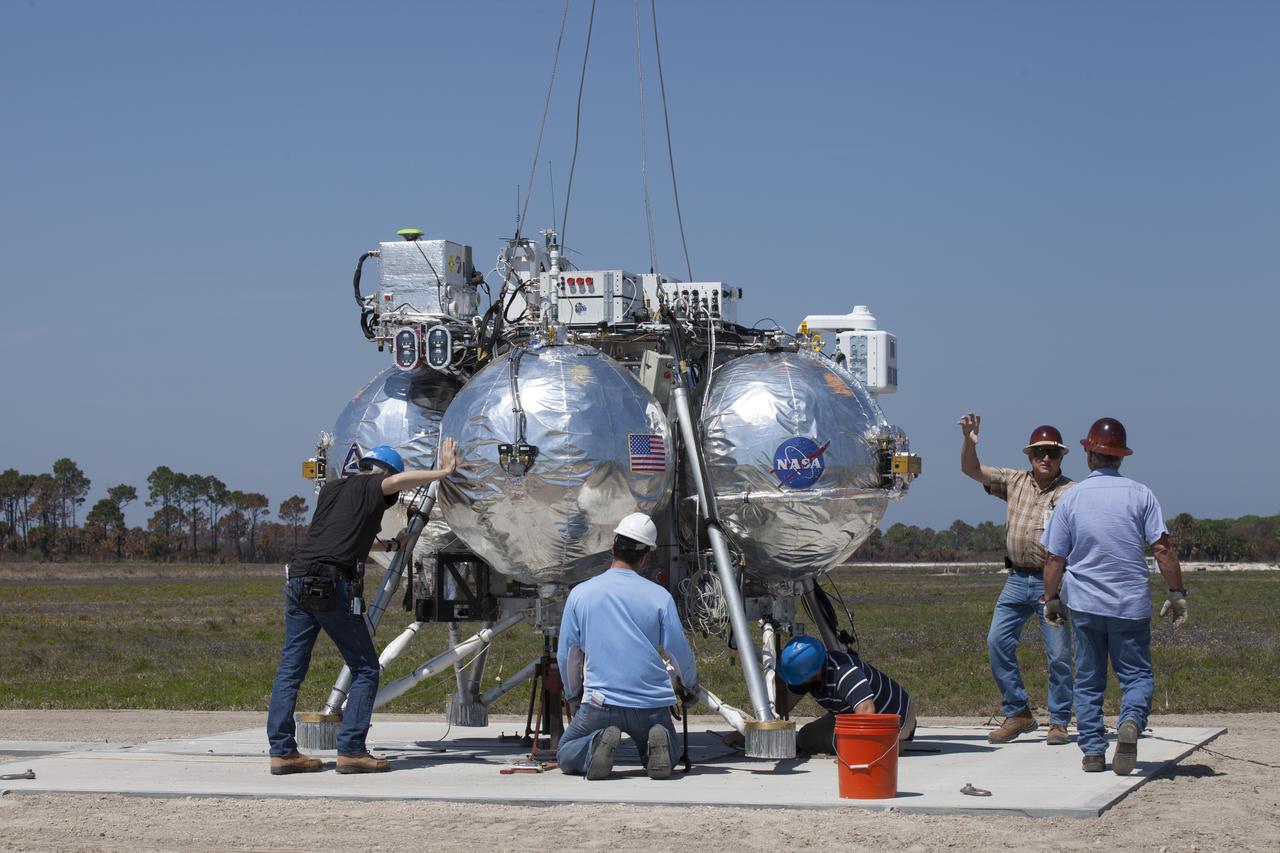 CAPE CANAVERAL, Fla. – Engineers and technicians prepare the Project Morpheus prototype lander for an automated landing and hazard avoidance technology, or ALHAT, and laser test at a new launch site at the north end of the Shuttle Landing Facility at NASA’s Kennedy Space Center in Florida. The launch pad was moved to a different location at the landing facility to support the next phase of flight testing. The seventh free flight test of Morpheus occurred on March 11. The 83-second test began at 3:41 p.m. EDT with the Morpheus lander launching from the ground over a flame trench and ascending to 580 feet. Morpheus then flew its fastest downrange trek at 30 mph, travelling farther than before, 837 feet. The lander performed a 42-foot divert to emulate a hazard avoidance maneuver before descending and touching down on Landing Site 2, at the northern landing pad inside the ALHAT hazard field. Morpheus landed within one foot of its intended target. Project Morpheus tests NASA’s ALHAT and an engine that runs on liquid oxygen and methane, or green propellants, into a fully-operational lander that could deliver cargo to other planetary surfaces. The landing facility provides the lander with the kind of field necessary for realistic testing, complete with rocks, craters and hazards to avoid. Morpheus’ ALHAT payload allows it to navigate to clear landing sites amidst rocks, craters and other hazards during its descent. Project Morpheus is being managed under the Advanced Exploration Systems, or AES, Division in NASA’s Human Exploration and Operations Mission Directorate. The efforts in AES pioneer new approaches for rapidly developing prototype systems, demonstrating key capabilities and validating operational concepts for future human missions beyond Earth orbit. For more information on Project Morpheus, visit http://morpheuslander.jsc.nasa.gov/. Photo credit: NASA/Kim Shiflett