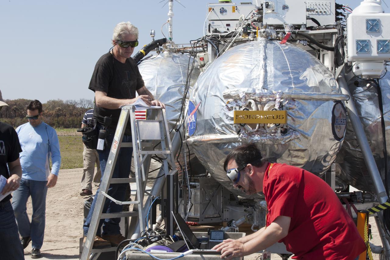 CAPE CANAVERAL, Fla. – Engineers and technicians prepare the Project Morpheus prototype lander for an automated landing and hazard avoidance technology, or ALHAT, and laser test at a new launch site at the north end of the Shuttle Landing Facility at NASA’s Kennedy Space Center in Florida. The launch pad was moved to a different location at the landing facility to support the next phase of flight testing. The seventh free flight test of Morpheus occurred on March 11. The 83-second test began at 3:41 p.m. EDT with the Morpheus lander launching from the ground over a flame trench and ascending to 580 feet. Morpheus then flew its fastest downrange trek at 30 mph, travelling farther than before, 837 feet. The lander performed a 42-foot divert to emulate a hazard avoidance maneuver before descending and touching down on Landing Site 2, at the northern landing pad inside the ALHAT hazard field. Morpheus landed within one foot of its intended target. Project Morpheus tests NASA’s ALHAT and an engine that runs on liquid oxygen and methane, or green propellants, into a fully-operational lander that could deliver cargo to other planetary surfaces. The landing facility provides the lander with the kind of field necessary for realistic testing, complete with rocks, craters and hazards to avoid. Morpheus’ ALHAT payload allows it to navigate to clear landing sites amidst rocks, craters and other hazards during its descent. Project Morpheus is being managed under the Advanced Exploration Systems, or AES, Division in NASA’s Human Exploration and Operations Mission Directorate. The efforts in AES pioneer new approaches for rapidly developing prototype systems, demonstrating key capabilities and validating operational concepts for future human missions beyond Earth orbit. For more information on Project Morpheus, visit http://morpheuslander.jsc.nasa.gov/. Photo credit: NASA/Kim Shiflett