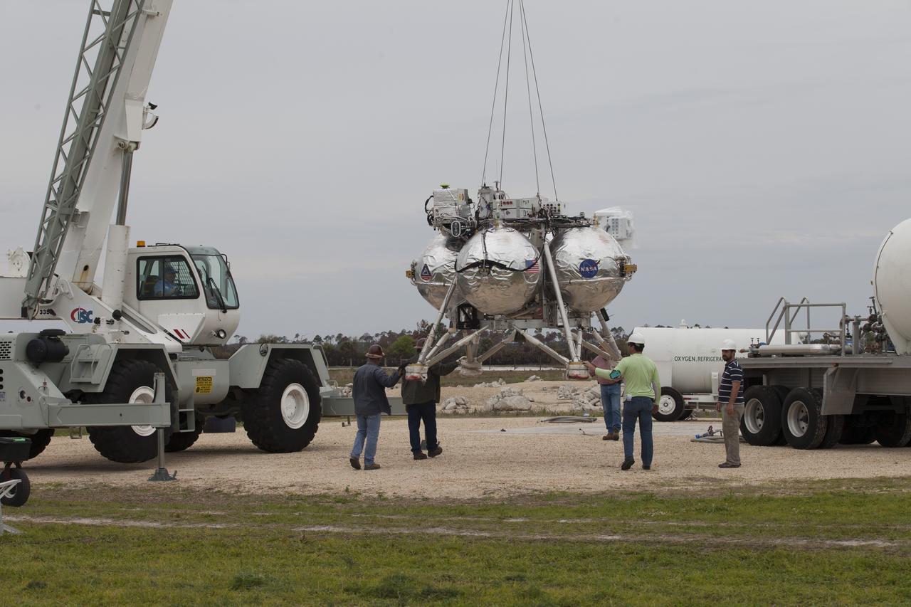 CAPE CANAVERAL, Fla. – Engineers and technicians monitor the progress as a crane lifts the Project Morpheus prototype lander off the ground for a tether test near a new launch site at the north end of the Shuttle Landing Facility at NASA's Kennedy Space Center in Florida. The launch pad was moved to a different location at the landing facility to support the next phase of flight testing. Project Morpheus tests NASA’s automated landing and hazard avoidance technology, or ALHAT, and an engine that runs on liquid oxygen and methane, or green propellants, into a fully-operational lander that could deliver cargo to other planetary surfaces. The landing facility provides the lander with the kind of field necessary for realistic testing, complete with rocks, craters and hazards to avoid. Morpheus’ ALHAT payload allows it to navigate to clear landing sites amidst rocks, craters and other hazards during its descent. Project Morpheus is being managed under the Advanced Exploration Systems, or AES, Division in NASA’s Human Exploration and Operations Mission Directorate. The efforts in AES pioneer new approaches for rapidly developing prototype systems, demonstrating key capabilities and validating operational concepts for future human missions beyond Earth orbit. For more information on Project Morpheus, visit http://morpheuslander.jsc.nasa.gov/. Photo credit: NASA/Ben Smegelsky