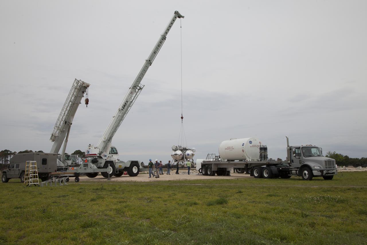CAPE CANAVERAL, Fla. – Engineers and technicians monitor the progress as a crane lifts the Project Morpheus prototype lander off the ground for a tether test near a new launch site at the north end of the Shuttle Landing Facility at NASA's Kennedy Space Center in Florida. The launch pad was moved to a different location at the landing facility to support the next phase of flight testing. Project Morpheus tests NASA’s automated landing and hazard avoidance technology, or ALHAT, and an engine that runs on liquid oxygen and methane, or green propellants, into a fully-operational lander that could deliver cargo to other planetary surfaces. The landing facility provides the lander with the kind of field necessary for realistic testing, complete with rocks, craters and hazards to avoid. Morpheus’ ALHAT payload allows it to navigate to clear landing sites amidst rocks, craters and other hazards during its descent. Project Morpheus is being managed under the Advanced Exploration Systems, or AES, Division in NASA’s Human Exploration and Operations Mission Directorate. The efforts in AES pioneer new approaches for rapidly developing prototype systems, demonstrating key capabilities and validating operational concepts for future human missions beyond Earth orbit. For more information on Project Morpheus, visit http://morpheuslander.jsc.nasa.gov/. Photo credit: NASA/Ben Smegelsky