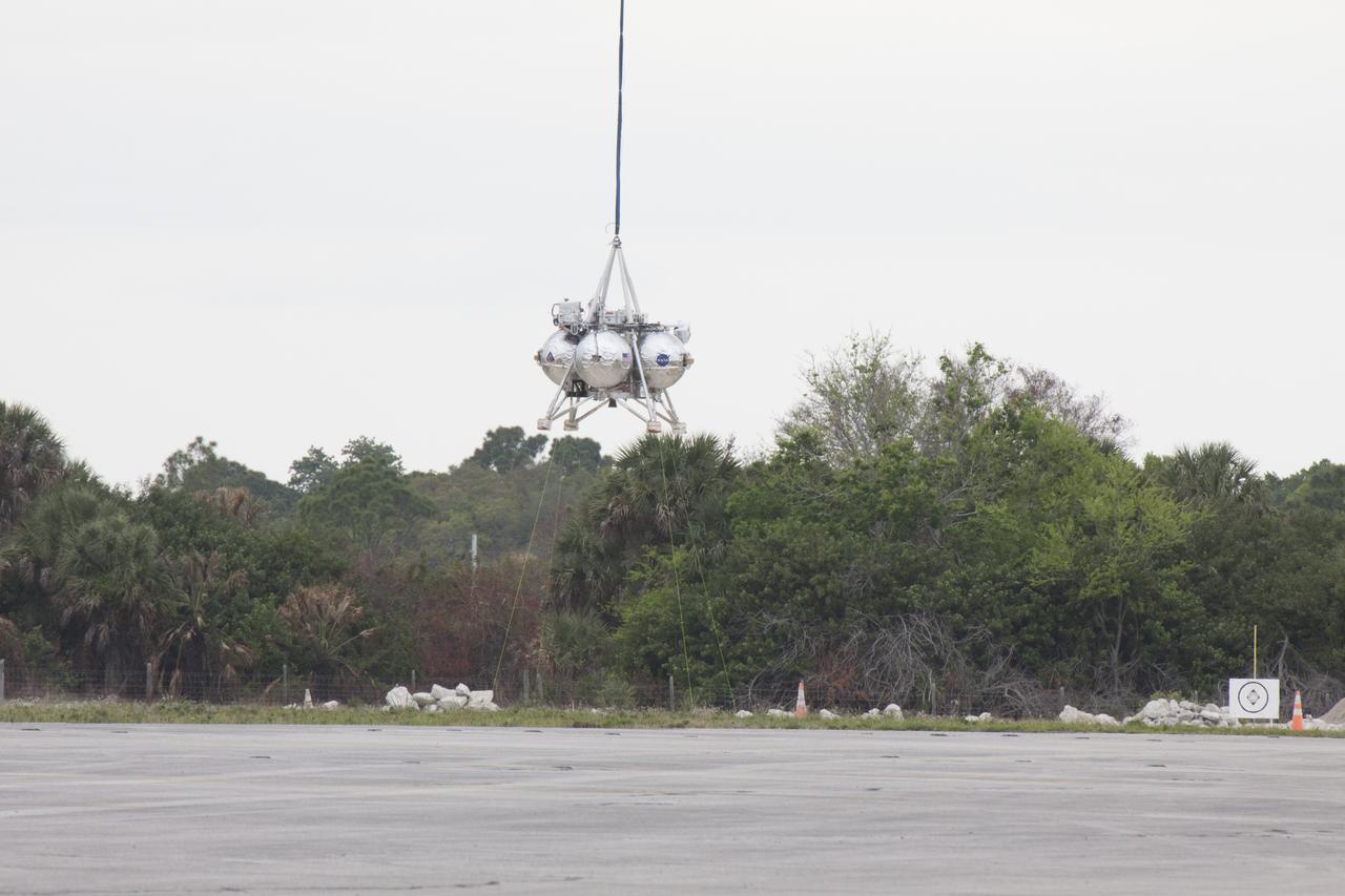 CAPE CANAVERAL, Fla. – NASA's Project Morpheus prototype lander is lifted by crane during a tethered test near a new launch site at the north end of the Shuttle Landing Facility at NASA's Kennedy Space Center in Florida. The launch pad was moved to a different location at the landing facility to support the next phase of flight testing. The test was performed to verify the lander's recently installed autonomous landing and hazard avoidance technology, or ALHAT, sensors and integration systems. During the test, Morpheus was lifted by crane to 20 feet for an engine firing of about 74 seconds and then lowered to the ground. With the successful completion of the test, the Morpheus project team will begin preparing for the first free flight test with ALHAT. Morpheus tests NASA’s ALHAT, and an engine that runs on liquid oxygen and methane, or green propellants, into a fully-operational lander that could deliver cargo to other planetary surfaces. The landing facility provides the lander with the kind of field necessary for realistic testing, complete with rocks, craters and hazards to avoid. Morpheus’ ALHAT payload allows it to navigate to clear landing sites amidst rocks, craters and other hazards during its descent. Project Morpheus is being managed under the Advanced Exploration Systems, or AES, Division in NASA’s Human Exploration and Operations Mission Directorate. The efforts in AES pioneer new approaches for rapidly developing prototype systems, demonstrating key capabilities and validating operational concepts for future human missions beyond Earth orbit. For more information on Project Morpheus, visit http://morpheuslander.jsc.nasa.gov/. Photo credit: NASA/Glenn Benson