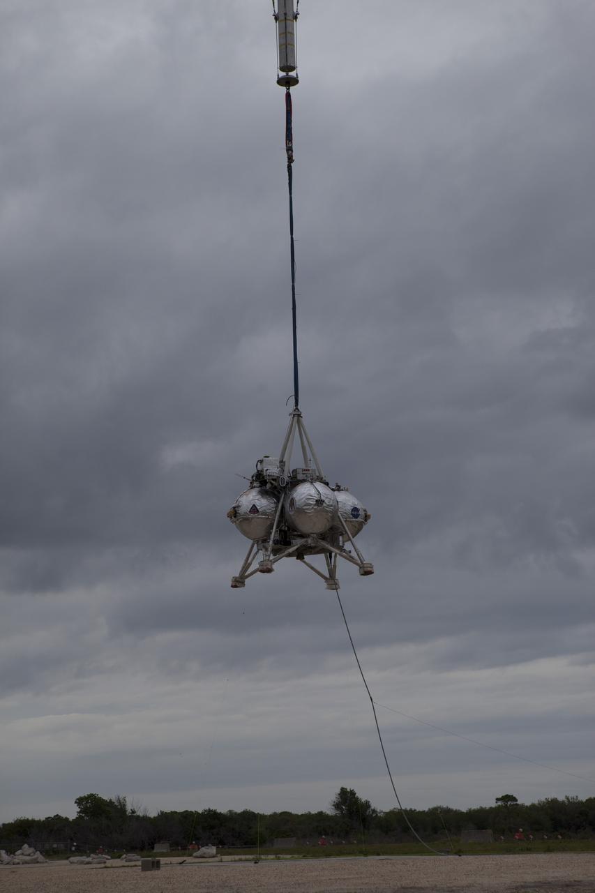 CAPE CANAVERAL, Fla. – NASA's Project Morpheus prototype lander is lifted by crane during a tethered test near a new launch site at the north end of the Shuttle Landing Facility at NASA's Kennedy Space Center in Florida. The launch pad was moved to a different location at the landing facility to support the next phase of flight testing. The test was performed to verify the lander's recently installed autonomous landing and hazard avoidance technology, or ALHAT, sensors and integration systems. During the test, Morpheus was lifted by crane to 20 feet for an engine firing of about 74 seconds and then lowered to the ground. With the successful completion of the test, the Morpheus project team will begin preparing for the first free flight test with ALHAT. Morpheus tests NASA’s ALHAT, and an engine that runs on liquid oxygen and methane, or green propellants, into a fully-operational lander that could deliver cargo to other planetary surfaces. The landing facility provides the lander with the kind of field necessary for realistic testing, complete with rocks, craters and hazards to avoid. Morpheus’ ALHAT payload allows it to navigate to clear landing sites amidst rocks, craters and other hazards during its descent. Project Morpheus is being managed under the Advanced Exploration Systems, or AES, Division in NASA’s Human Exploration and Operations Mission Directorate. The efforts in AES pioneer new approaches for rapidly developing prototype systems, demonstrating key capabilities and validating operational concepts for future human missions beyond Earth orbit. For more information on Project Morpheus, visit http://morpheuslander.jsc.nasa.gov/. Photo credit: NASA/Glenn Benson