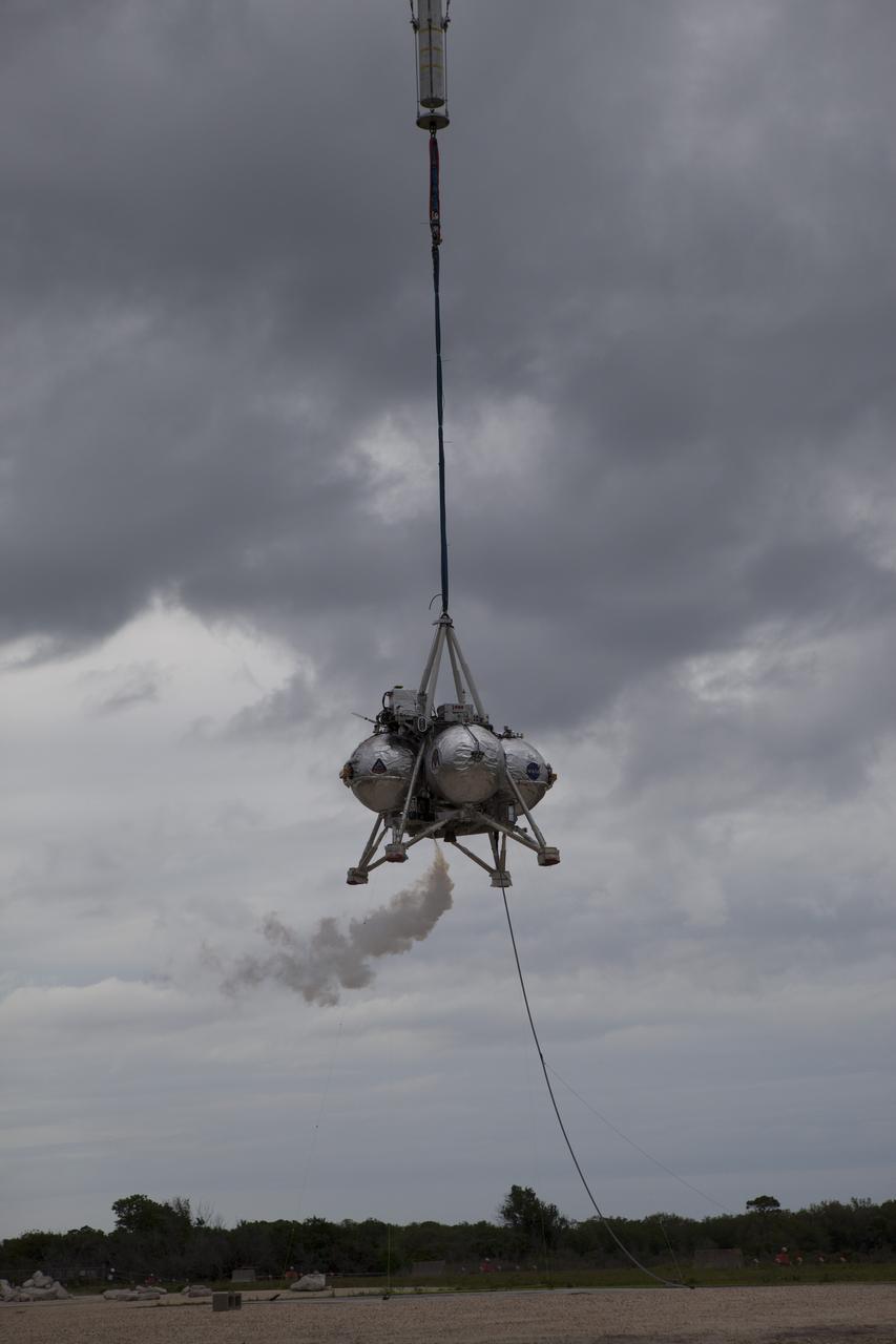 CAPE CANAVERAL, Fla. – NASA's Project Morpheus prototype lander is lifted by crane during a tethered test near a new launch site at the north end of the Shuttle Landing Facility at NASA's Kennedy Space Center in Florida. The launch pad was moved to a different location at the landing facility to support the next phase of flight testing. The test was performed to verify the lander's recently installed autonomous landing and hazard avoidance technology, or ALHAT, sensors and integration systems. During the test, Morpheus was lifted by crane to 20 feet for an engine firing of about 74 seconds and then lowered to the ground. With the successful completion of the test, the Morpheus project team will begin preparing for the first free flight test with ALHAT. Morpheus tests NASA’s ALHAT, and an engine that runs on liquid oxygen and methane, or green propellants, into a fully-operational lander that could deliver cargo to other planetary surfaces. The landing facility provides the lander with the kind of field necessary for realistic testing, complete with rocks, craters and hazards to avoid. Morpheus’ ALHAT payload allows it to navigate to clear landing sites amidst rocks, craters and other hazards during its descent. Project Morpheus is being managed under the Advanced Exploration Systems, or AES, Division in NASA’s Human Exploration and Operations Mission Directorate. The efforts in AES pioneer new approaches for rapidly developing prototype systems, demonstrating key capabilities and validating operational concepts for future human missions beyond Earth orbit. For more information on Project Morpheus, visit http://morpheuslander.jsc.nasa.gov/. Photo credit: NASA/Glenn Benson