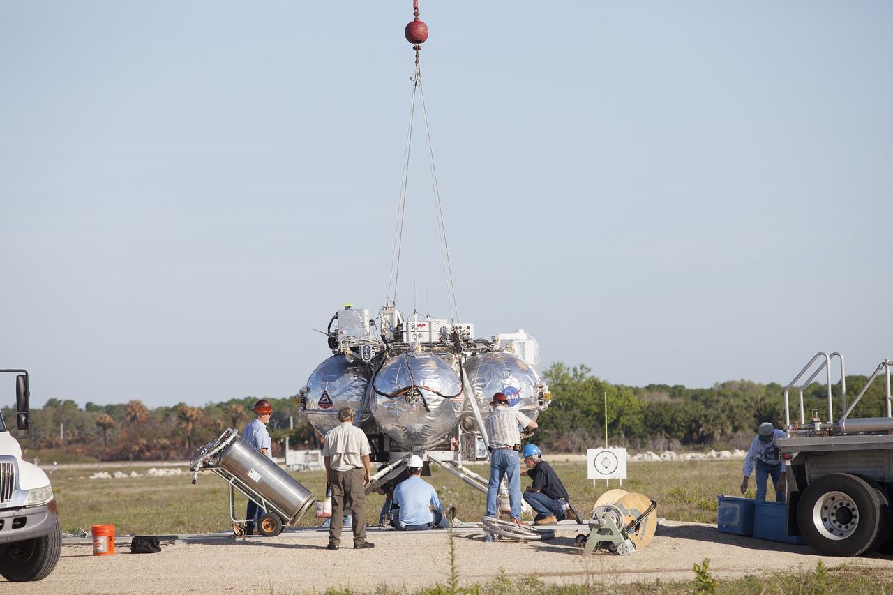 CAPE CANAVERAL, Fla. – Engineers and technicians prepare NASA's Project Morpheus prototype lander for a free flight test at a new launch site at the north end of the Shuttle Landing Facility at NASA’s Kennedy Space Center in Florida. The 96-second test began at 4:21 p.m. EDT with the Morpheus lander launching from the ground over the flame trench and ascending more than 800 feet at a peak speed of 36 mph. The vehicle with its recently installed autonomous landing and hazard avoidance technology, or ALHAT, sensors surveyed the hazard field to determine safe landing sites. Morpheus then flew forward and downward covering 1,300 feet while performing a 78-foot divert to simulate a hazard avoidance maneuver. The lander descended and landed on a dedicated pad inside the ALHAT field. Project Morpheus tests NASA’s ALHAT, and an engine that runs on liquid oxygen and methane, or green propellants, into a fully-operational lander that could deliver cargo to other planetary surfaces. The landing facility provides the lander with the kind of field necessary for realistic testing, complete with rocks, craters and hazards to avoid. Morpheus’ ALHAT payload allows it to navigate to clear landing sites amidst rocks, craters and other hazards during its descent. Project Morpheus is being managed under the Advanced Exploration Systems, or AES, Division in NASA’s Human Exploration and Operations Mission Directorate. The efforts in AES pioneer new approaches for rapidly developing prototype systems, demonstrating key capabilities and validating operational concepts for future human missions beyond Earth orbit. For more information on Project Morpheus, visit http://morpheuslander.jsc.nasa.gov/. Photo credit: NASA/Frankie Martin