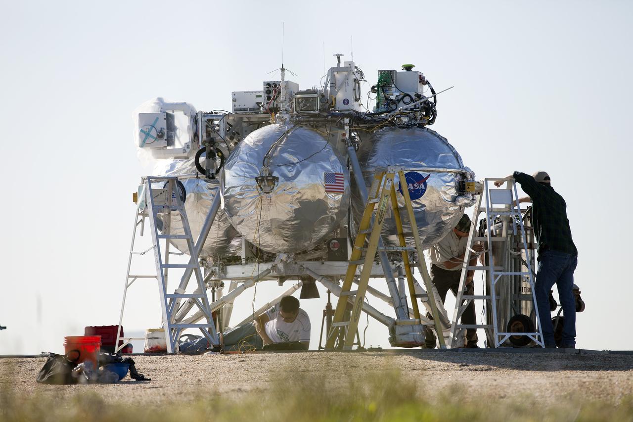 CAPE CANAVERAL, Fla. – Engineers and technicians prepare NASA's Project Morpheus prototype lander for a free flight test at a new launch site at the north end of the Shuttle Landing Facility at NASA’s Kennedy Space Center in Florida. The 96-second test began at 4:21 p.m. EDT with the Morpheus lander launching from the ground over the flame trench and ascending more than 800 feet at a peak speed of 36 mph. The vehicle with its recently installed autonomous landing and hazard avoidance technology, or ALHAT, sensors surveyed the hazard field to determine safe landing sites. Morpheus then flew forward and downward covering 1,300 feet while performing a 78-foot divert to simulate a hazard avoidance maneuver. The lander descended and landed on a dedicated pad inside the ALHAT field. Project Morpheus tests NASA’s ALHAT, and an engine that runs on liquid oxygen and methane, or green propellants, into a fully-operational lander that could deliver cargo to other planetary surfaces.    The landing facility provides the lander with the kind of field necessary for realistic testing, complete with rocks, craters and hazards to avoid. Morpheus’ ALHAT payload allows it to navigate to clear landing sites amidst rocks, craters and other hazards during its descent. Project Morpheus is being managed under the Advanced Exploration Systems, or AES, Division in NASA’s Human Exploration and Operations Mission Directorate. The efforts in AES pioneer new approaches for rapidly developing prototype systems, demonstrating key capabilities and validating operational concepts for future human missions beyond Earth orbit. For more information on Project Morpheus, visit http://morpheuslander.jsc.nasa.gov/.  Photo credit: NASA/Frankie Martin