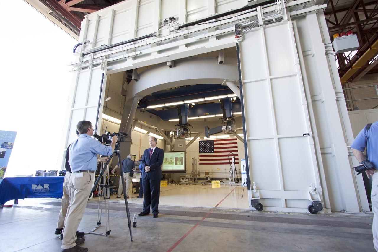 CAPE CANAVERAL, Fla. – Tom Engler, deputy director of the Center Planning and Development Directorate at Kennedy Space Center, speaks to members of the media during an Open House event at Hangar N at Cape Canaveral Air Force Station in Florida, to celebrate the one-year anniversary of PaR Systems' partnership with Kennedy. Under a 15-year lease agreement, PaR Systems is utilizing Hangar N and its unique nondestructive testing equipment. Behind Engler is the robotic inspection cell that contains an automated X-ray system once used to scan the aft skirts of the solid rocket boosters for the space shuttle.     The partnership agreement was established by Kennedy's Center Planning and Development Directorate. The agreement is just one example of the types of partnerships that Kennedy is seeking to create a multi-user spaceport.  Photo credit: NASA/Cory Huston