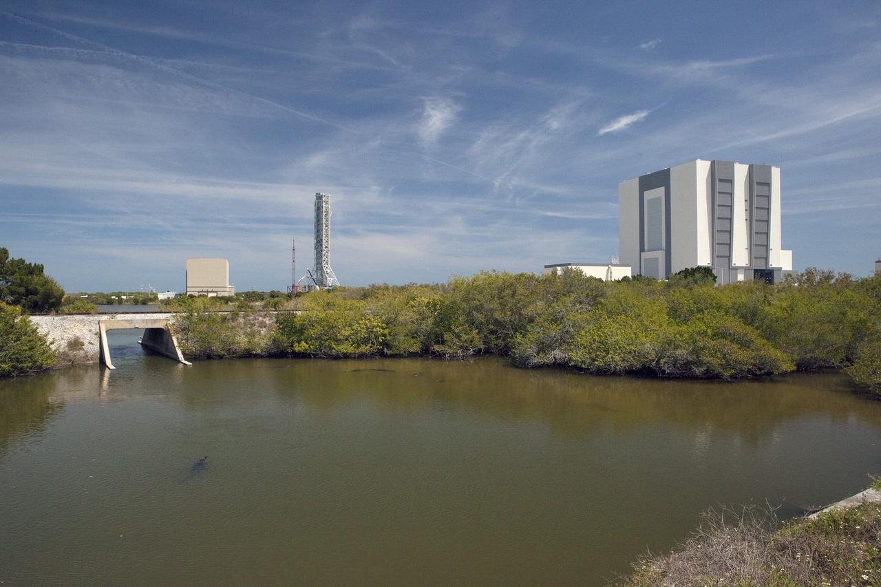 CAPE CANAVERAL, Fla. – Manatees and alligators gather in a creek at Kennedy Space Center's Launch Complex 39 area. In the background from left to right are the Rotation, Processing and Surge Facility, mobile launcher and Vehicle Assembly Building.    The center shares a boundary with the Merritt Island National Wildlife Refuge, which encompasses 140,000 acres that provide a habitat for more than 330 species of birds, 31 mammals, 117 fishes, and 65 amphibians and reptiles. Photo credit: NASA/Daniel Casper
