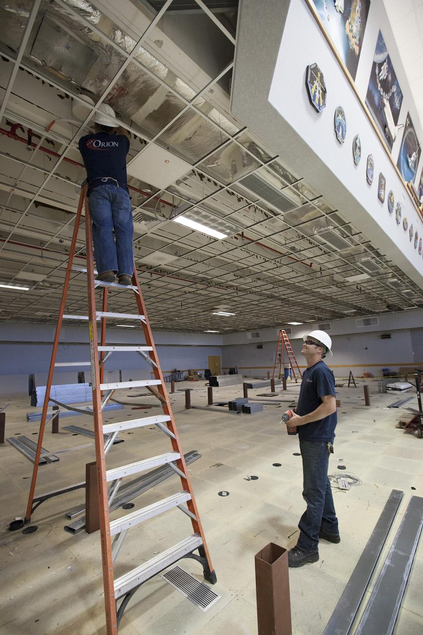 CAPE CANAVERAL, Fla. – Inside Firing Room 4 in the Launch Control Center at NASA's Kennedy Space Center in Florida, construction workers make adjustments to conduit in the ceiling. The Ground Systems Development and Operations Program is overseeing efforts to create a new firing room based on a multi-user concept that will support NASA and commercial launch needs. The main floor consoles, cabling and wires below the floor and the ceiling tiles above have been removed. Sub flooring has been installed and the room is marked off to create four separate rooms on the main floor. In view along the soffit are space shuttle launch plaques for 21 missions launched from Firing Room 4. The design of Firing Room 4 will incorporate five control room areas that are flexible to meet current and future NASA and commercial user requirements. The equipment and most of the consoles from Firing Room 4 were moved to Firing Room 2 for possible future reuse. Photo credit: NASA/Ben Smegelsky