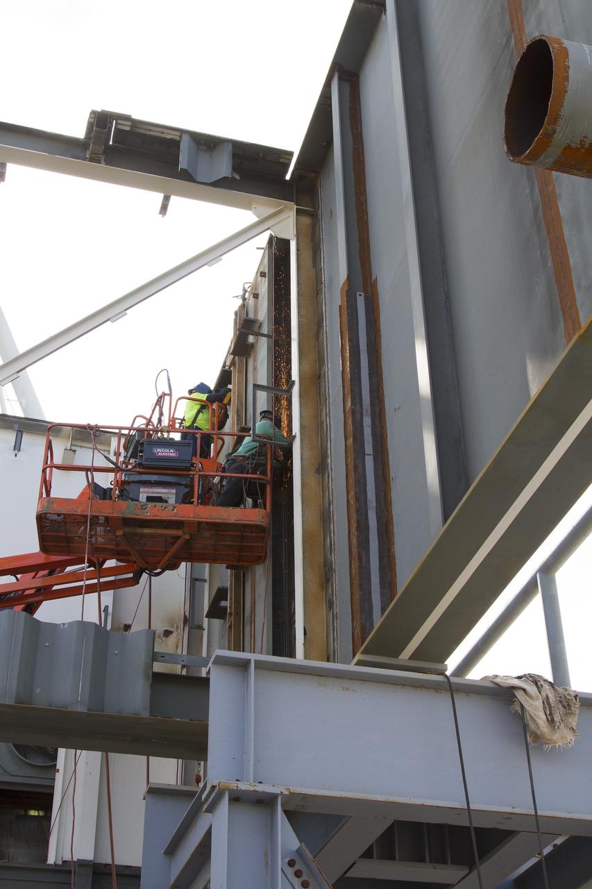 CAPE CANAVERAL, Fla. – Modifications continue on the Mobile Launcher, or ML, at the Mobile Launcher Park Site at NASA’s Kennedy Space Center in Florida. Construction workers on lifts perform welding work on the exterior of the ML.    In 2013, the agency awarded a contract to J.P. Donovan Construction Inc. of Rockledge, Fla., to modify the ML, which is one of the key elements of ground support equipment that is being upgraded by the Ground Systems Development and Operations Program office at Kennedy. The ML will carry the SLS rocket and Orion spacecraft to Launch Pad 39B for its first mission, Exploration Mission 1, in 2017. Photo credit: NASA/Cory Huston
