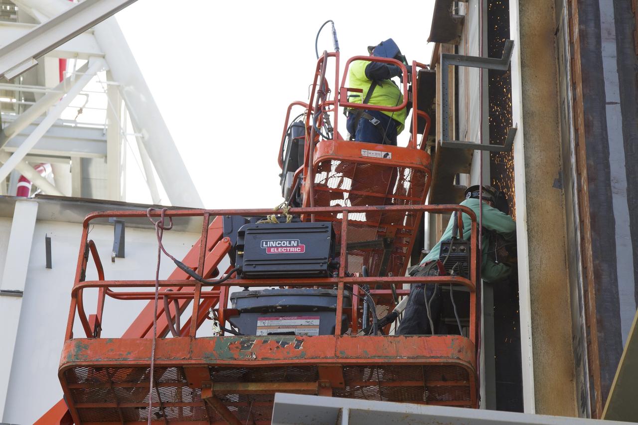 CAPE CANAVERAL, Fla. – Modifications continue on the Mobile Launcher, or ML, at the Mobile Launcher Park Site at NASA’s Kennedy Space Center in Florida. Construction workers on lifts perform welding work on the exterior of the ML.    In 2013, the agency awarded a contract to J.P. Donovan Construction Inc. of Rockledge, Fla., to modify the ML, which is one of the key elements of ground support equipment that is being upgraded by the Ground Systems Development and Operations Program office at Kennedy. The ML will carry the SLS rocket and Orion spacecraft to Launch Pad 39B for its first mission, Exploration Mission 1, in 2017. Photo credit: NASA/Cory Huston