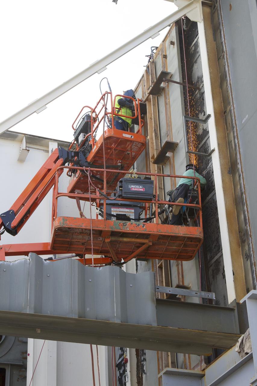 CAPE CANAVERAL, Fla. – Modifications continue on the Mobile Launcher, or ML, at the Mobile Launcher Park Site at NASA’s Kennedy Space Center in Florida. Construction workers on lifts perform welding work on the exterior of the ML.    In 2013, the agency awarded a contract to J.P. Donovan Construction Inc. of Rockledge, Fla., to modify the ML, which is one of the key elements of ground support equipment that is being upgraded by the Ground Systems Development and Operations Program office at Kennedy. The ML will carry the SLS rocket and Orion spacecraft to Launch Pad 39B for its first mission, Exploration Mission 1, in 2017. Photo credit: NASA/Cory Huston