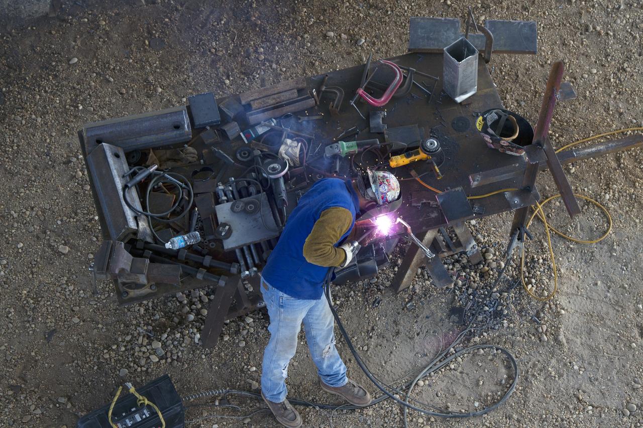 CAPE CANAVERAL, Fla. – Modifications continue on the Mobile Launcher, or ML, at the Mobile Launcher Park Site at NASA’s Kennedy Space Center in Florida. In this aerial view looking down from the surface of the ML, a construction worker welds a section of metal for installation on the ML.    In 2013, the agency awarded a contract to J.P. Donovan Construction Inc. of Rockledge, Fla., to modify the ML, which is one of the key elements of ground support equipment that is being upgraded by the Ground Systems Development and Operations Program office at Kennedy. The ML will carry the SLS rocket and Orion spacecraft to Launch Pad 39B for its first mission, Exploration Mission 1, in 2017. Photo credit: NASA/Cory Huston