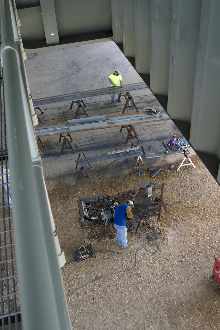 CAPE CANAVERAL, Fla. – Modifications continue on the Mobile Launcher, or ML, at the Mobile Launcher Park Site at NASA’s Kennedy Space Center in Florida. In this aerial view looking down from the ML, construction workers prepare sections of metal for installation.    In 2013, the agency awarded a contract to J.P. Donovan Construction Inc. of Rockledge, Fla., to modify the ML, which is one of the key elements of ground support equipment that is being upgraded by the Ground Systems Development and Operations Program office at Kennedy. The ML will carry the SLS rocket and Orion spacecraft to Launch Pad 39B for its first mission, Exploration Mission 1, in 2017. Photo credit: NASA/Cory Huston