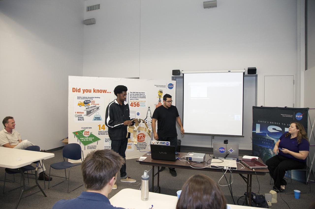 CAPE CANAVERAL, Fla. - SpaceWear team members Keith Hargett, left, and Alejandro Velasco explain their entry in the International Space Apps Challenge to an audience in the Center for Space Education at the Kennedy Space Center Visitor Complex in Florida. In the audience at left is NASA Ground Systems Development and Operations Program Manager Michael Bolger. Caley Burke, the NASA event organizer lead, is at right.      Kennedy Space Center hosted one of the over 90 locations around the world where participants congregated for the attempt to design innovative solutions for global challenges over a 48-hour period. This year's development marathon focused on five NASA mission areas: Asteroids, Earth Watch, Human Spaceflight, Robotics, and Technology in Space. Three of this year’s challenges were developed by KSC employees: Space Wearables: Fashion Designer to Astronauts, Growing Food for a Martian Table, and Asteroid Prospector. The winners selected in 2014 at Kennedy were Astronaut Resource Managing System, or ARMS, for Best Use of Data and SpaceWear for Best Use of Hardware. ARMS also took the People's Choice Award. For more information, visit https://2014.spaceappschallenge.org.  Photo credit: NASA/Daniel Casper