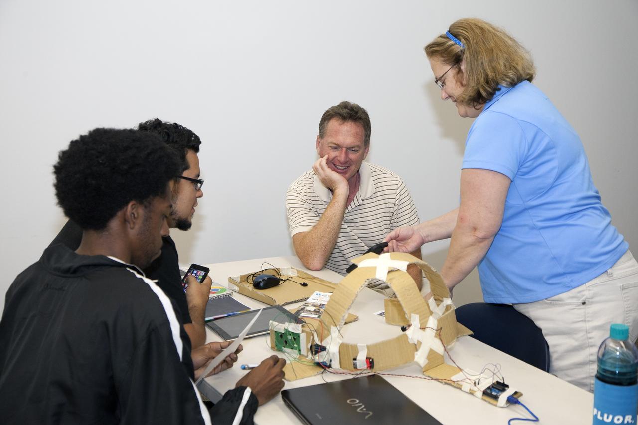 CAPE CANAVERAL, Fla. - SpaceWear team members Keith Hargett, left, and Alejandro Velasco demonstrate their entry in the International Space Apps Challenge to NASA Ground Systems Development and Operation Program Manager Michael Bolger and NASA's Lisa Singleton in the Center for Space Education at the Kennedy Space Center Visitor Complex in Florida.      Kennedy Space Center hosted one of the over 90 locations around the world where participants congregated for the attempt to design innovative solutions for global challenges over a 48-hour period. This year's development marathon focused on five NASA mission areas: Asteroids, Earth Watch, Human Spaceflight, Robotics, and Technology in Space. Three of this year’s challenges were developed by KSC employees: Space Wearables: Fashion Designer to Astronauts, Growing Food for a Martian Table, and Asteroid Prospector. The winners selected in 2014 at Kennedy were Astronaut Resource Managing System, or ARMS, for Best Use of Data and SpaceWear for Best Use of Hardware. ARMS also took the People's Choice Award. For more information, visit https://2014.spaceappschallenge.org.  Photo credit: NASA/Daniel Casper