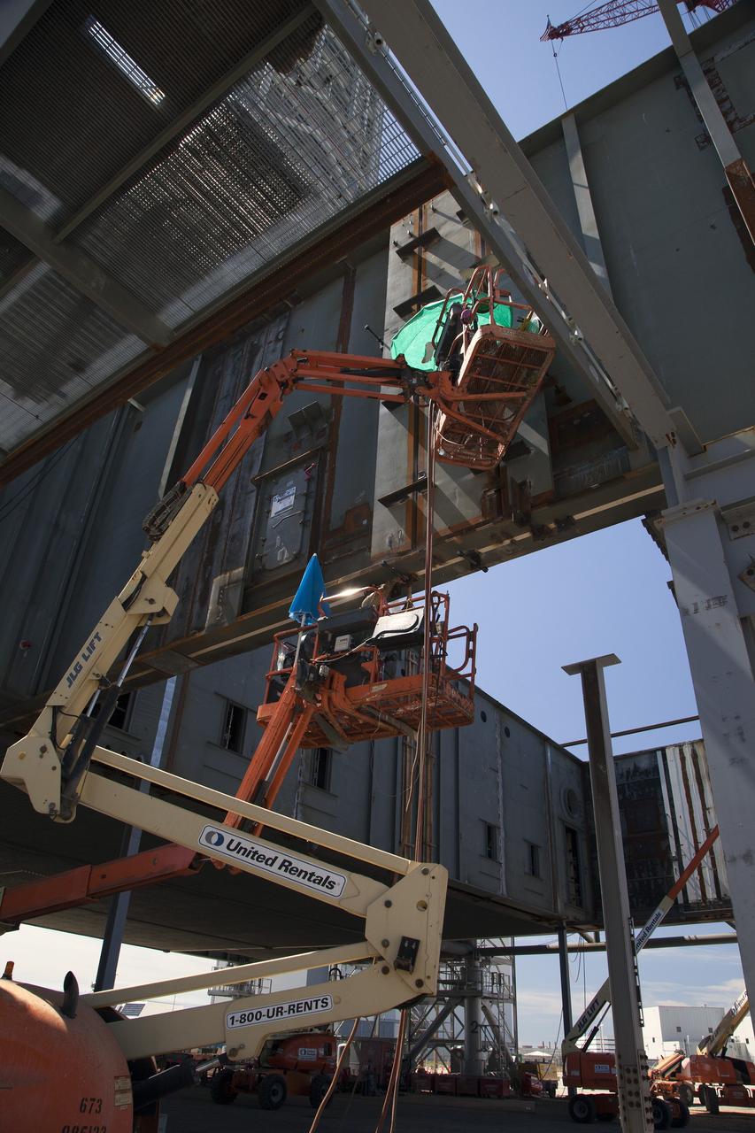 CAPE CANAVERAL, Fla. -- Modifications continue on the Mobile Launcher, or ML, at the Mobile Launcher Park Site at NASA’s Kennedy Space Center in Florida. Construction worker on lifts are preparing to cut and weld sections of the metal walls on the exterior of the ML.     In 2013, the agency awarded a contract to J.P. Donovan Construction Inc. of Rockledge, Fla., to modify the ML, which is one of the key elements of ground support equipment that is being upgraded by the Ground Systems Development and Operations Program office at Kennedy. The ML will carry the SLS rocket and Orion spacecraft to Launch Pad 39B for its first mission, Exploration Mission 1, in 2017. Photo credit: NASA/Daniel Casper
