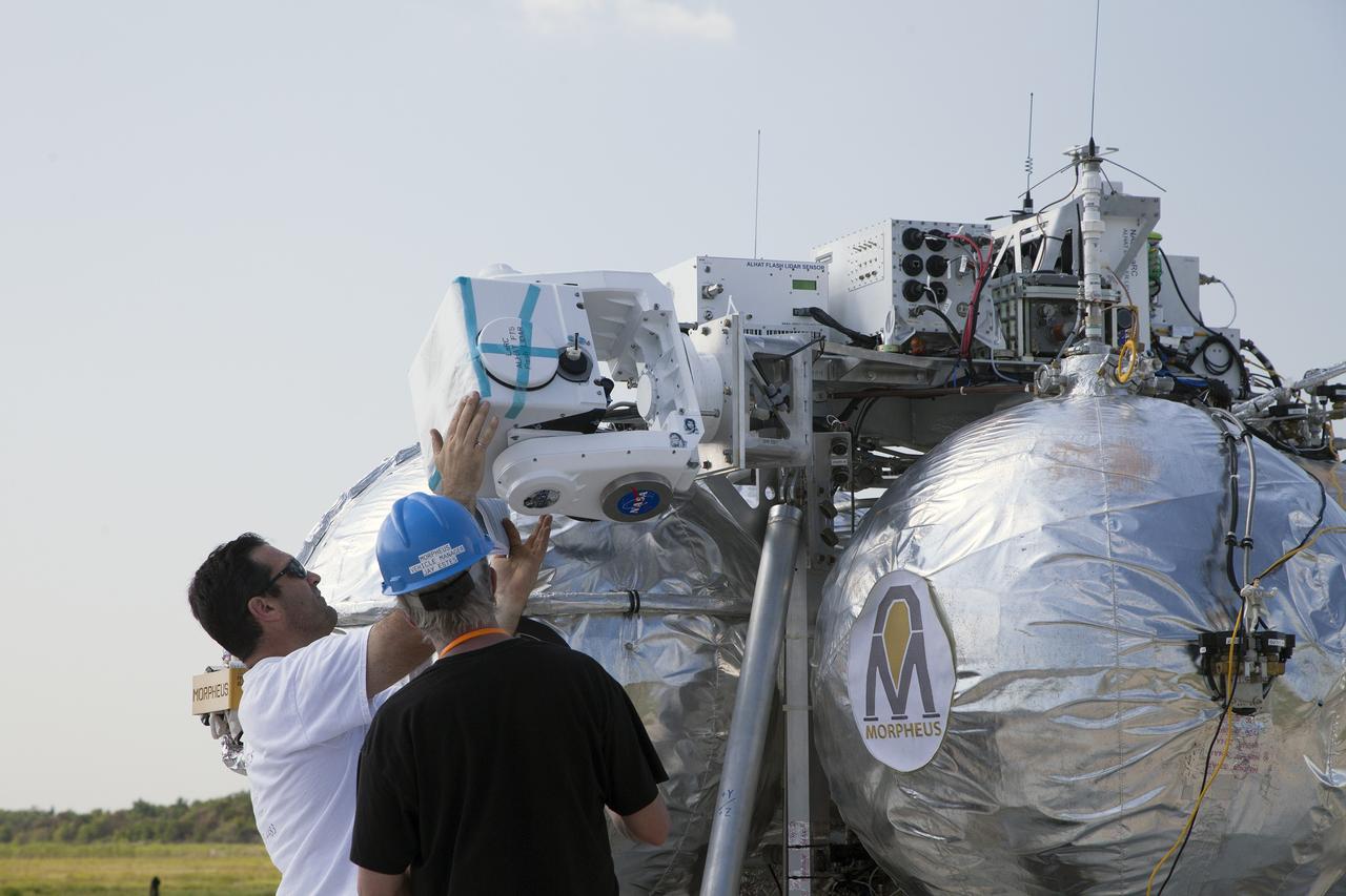 CAPE CANAVERAL, Fla. – Technicians check the systems on NASA's Project Morpheus prototype lander in preparation for a free-flight test from a new launch pad at the north end of the Shuttle Landing Facility at NASA's Kennedy Space Center in Florida. The 98-second test began at 3:20 p.m. EDT with the Morpheus lander launching from the ground over a flame trench and ascending more than 800 feet at a peak speed of 36 mph. The vehicle, with its recently installed autonomous landing and hazard avoidance technology ALHAT sensors, surveyed the hazard field to determine safe landing sites. Morpheus then flew forward and downward covering approximately 1300 feet while performing a 78-foot divert to simulate a hazard avoidance maneuver. The lander then descended and landed on a dedicated pad inside the autonomous landing and hazard avoidance technology hazard field. Project Morpheus tests NASA’s ALHAT and an engine that runs on liquid oxygen and methane, which are green propellants. These new capabilities could be used in future efforts to deliver cargo to planetary surfaces. The landing facility provides the lander with the kind of field necessary for realistic testing, complete with rocks, craters and hazards to avoid. Morpheus’ ALHAT payload allows it to navigate to clear landing sites amidst rocks, craters and other hazards during its descent. Project Morpheus is being managed under the Advanced Exploration Systems, or AES, Division in NASA’s Human Exploration and Operations Mission Directorate. The efforts in AES pioneer new approaches for rapidly developing prototype systems, demonstrating key capabilities and validating operational concepts for future human missions beyond Earth orbit. For more information on Project Morpheus, visit http://morpheuslander.jsc.nasa.gov/. Photo credit: NASA/Daniel Casper