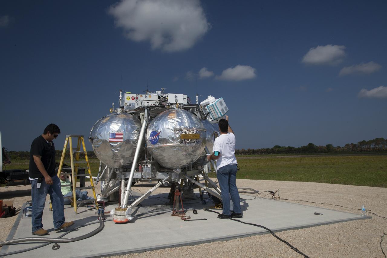 CAPE CANAVERAL, Fla. – Technicians check the systems on NASA's Project Morpheus prototype lander in preparation for a free-flight test from a new launch pad at the north end of the Shuttle Landing Facility at NASA's Kennedy Space Center in Florida. The 98-second test began at 3:20 p.m. EDT with the Morpheus lander launching from the ground over a flame trench and ascending more than 800 feet at a peak speed of 36 mph. The vehicle, with its recently installed autonomous landing and hazard avoidance technology ALHAT sensors, surveyed the hazard field to determine safe landing sites. Morpheus then flew forward and downward covering approximately 1300 feet while performing a 78-foot divert to simulate a hazard avoidance maneuver. The lander then descended and landed on a dedicated pad inside the autonomous landing and hazard avoidance technology hazard field. Project Morpheus tests NASA’s ALHAT and an engine that runs on liquid oxygen and methane, which are green propellants. These new capabilities could be used in future efforts to deliver cargo to planetary surfaces.      The landing facility provides the lander with the kind of field necessary for realistic testing, complete with rocks, craters and hazards to avoid. Morpheus’ ALHAT payload allows it to navigate to clear landing sites amidst rocks, craters and other hazards during its descent. Project Morpheus is being managed under the Advanced Exploration Systems, or AES, Division in NASA’s Human Exploration and Operations Mission Directorate. The efforts in AES pioneer new approaches for rapidly developing prototype systems, demonstrating key capabilities and validating operational concepts for future human missions beyond Earth orbit. For more information on Project Morpheus, visit http://morpheuslander.jsc.nasa.gov/.  Photo credit: NASA/Daniel Casper