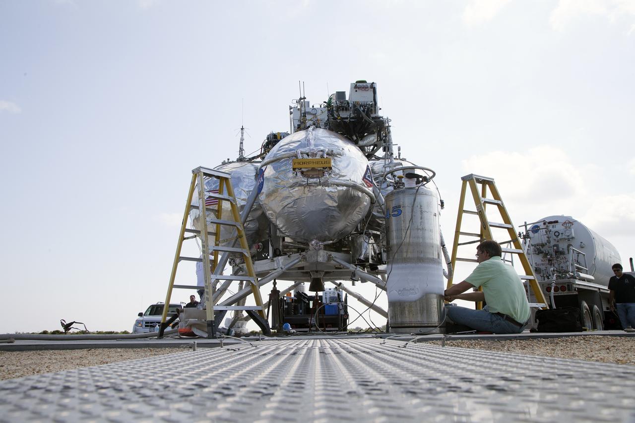 CAPE CANAVERAL, Fla. – Technicians check the systems on NASA's Project Morpheus prototype lander in preparation for a free-flight test from a new launch pad at the north end of the Shuttle Landing Facility at NASA's Kennedy Space Center in Florida. The 98-second test began at 3:20 p.m. EDT with the Morpheus lander launching from the ground over a flame trench and ascending more than 800 feet at a peak speed of 36 mph. The vehicle, with its recently installed autonomous landing and hazard avoidance technology ALHAT sensors, surveyed the hazard field to determine safe landing sites. Morpheus then flew forward and downward covering approximately 1300 feet while performing a 78-foot divert to simulate a hazard avoidance maneuver. The lander then descended and landed on a dedicated pad inside the autonomous landing and hazard avoidance technology hazard field. Project Morpheus tests NASA’s ALHAT and an engine that runs on liquid oxygen and methane, which are green propellants. These new capabilities could be used in future efforts to deliver cargo to planetary surfaces.      The landing facility provides the lander with the kind of field necessary for realistic testing, complete with rocks, craters and hazards to avoid. Morpheus’ ALHAT payload allows it to navigate to clear landing sites amidst rocks, craters and other hazards during its descent. Project Morpheus is being managed under the Advanced Exploration Systems, or AES, Division in NASA’s Human Exploration and Operations Mission Directorate. The efforts in AES pioneer new approaches for rapidly developing prototype systems, demonstrating key capabilities and validating operational concepts for future human missions beyond Earth orbit. For more information on Project Morpheus, visit http://morpheuslander.jsc.nasa.gov/.  Photo credit: NASA/Daniel Casper