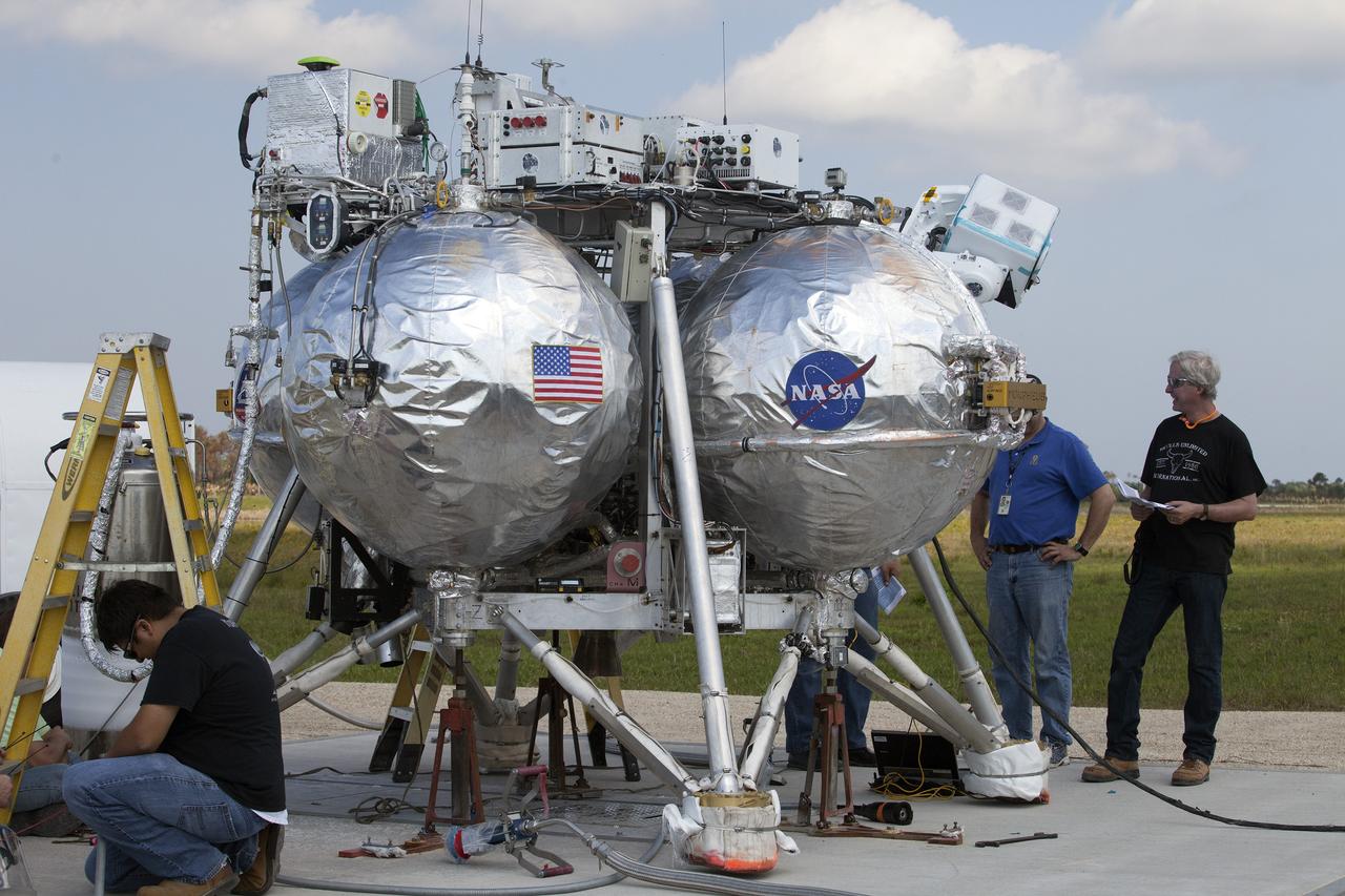 CAPE CANAVERAL, Fla. – Technicians and engineers check the systems on NASA's Project Morpheus prototype lander in preparation for a free flight test from a new launch pad at the north end of the Shuttle Landing Facility at NASA's Kennedy Space Center in Florida. The 98-second test began at 3:20 p.m. EDT with the Morpheus lander launching from the ground over a flame trench and ascending more than 800 feet at a peak speed of 36 mph. The vehicle, with its recently installed autonomous landing and hazard avoidance technology ALHAT sensors, surveyed the hazard field to determine safe landing sites. Morpheus then flew forward and downward covering approximately 1300 feet while performing a 78-foot divert to simulate a hazard avoidance maneuver. The lander then descended and landed on a dedicated pad inside the autonomous landing and hazard avoidance technology hazard field. Project Morpheus tests NASA’s ALHAT and an engine that runs on liquid oxygen and methane, which are green propellants. These new capabilities could be used in future efforts to deliver cargo to planetary surfaces. The landing facility provides the lander with the kind of field necessary for realistic testing, complete with rocks, craters and hazards to avoid. Morpheus’ ALHAT payload allows it to navigate to clear landing sites amidst rocks, craters and other hazards during its descent. Project Morpheus is being managed under the Advanced Exploration Systems, or AES, Division in NASA’s Human Exploration and Operations Mission Directorate. The efforts in AES pioneer new approaches for rapidly developing prototype systems, demonstrating key capabilities and validating operational concepts for future human missions beyond Earth orbit. For more information on Project Morpheus, visit http://morpheuslander.jsc.nasa.gov/. Photo credit: NASA/Daniel Casper