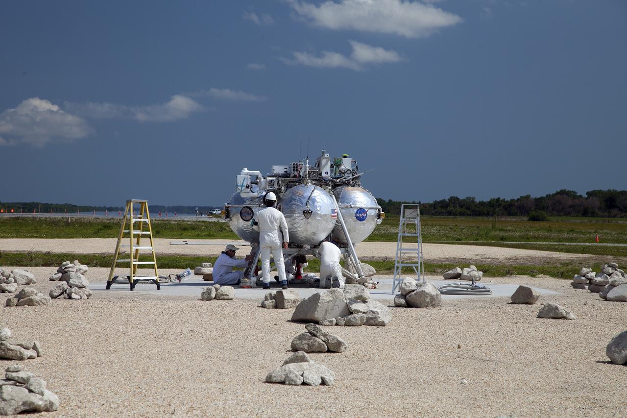 CAPE CANAVERAL, Fla. – Technicians and engineers prepare NASA's Project Morpheus prototype lander for a free flight test from a new launch pad at the north end of the Shuttle Landing Facility at NASA's Kennedy Space Center in Florida. The 98-second test began at 3:20 p.m. EDT with the Morpheus lander launching from the ground over a flame trench and ascending more than 800 feet at a peak speed of 36 mph. The vehicle, with its recently installed autonomous landing and hazard avoidance technology ALHAT sensors, surveyed the hazard field to determine safe landing sites. Morpheus then flew forward and downward covering approximately 1300 feet while performing a 78-foot divert to simulate a hazard avoidance maneuver. The lander then descended and landed on a dedicated pad inside the autonomous landing and hazard avoidance technology hazard field. Project Morpheus tests NASA’s ALHAT and an engine that runs on liquid oxygen and methane, which are green propellants. These new capabilities could be used in future efforts to deliver cargo to planetary surfaces. The landing facility provides the lander with the kind of field necessary for realistic testing, complete with rocks, craters and hazards to avoid. Morpheus’ ALHAT payload allows it to navigate to clear landing sites amidst rocks, craters and other hazards during its descent. Project Morpheus is being managed under the Advanced Exploration Systems, or AES, Division in NASA’s Human Exploration and Operations Mission Directorate. The efforts in AES pioneer new approaches for rapidly developing prototype systems, demonstrating key capabilities and validating operational concepts for future human missions beyond Earth orbit. For more information on Project Morpheus, visit http://morpheuslander.jsc.nasa.gov/. Photo credit: NASA/Daniel Casper