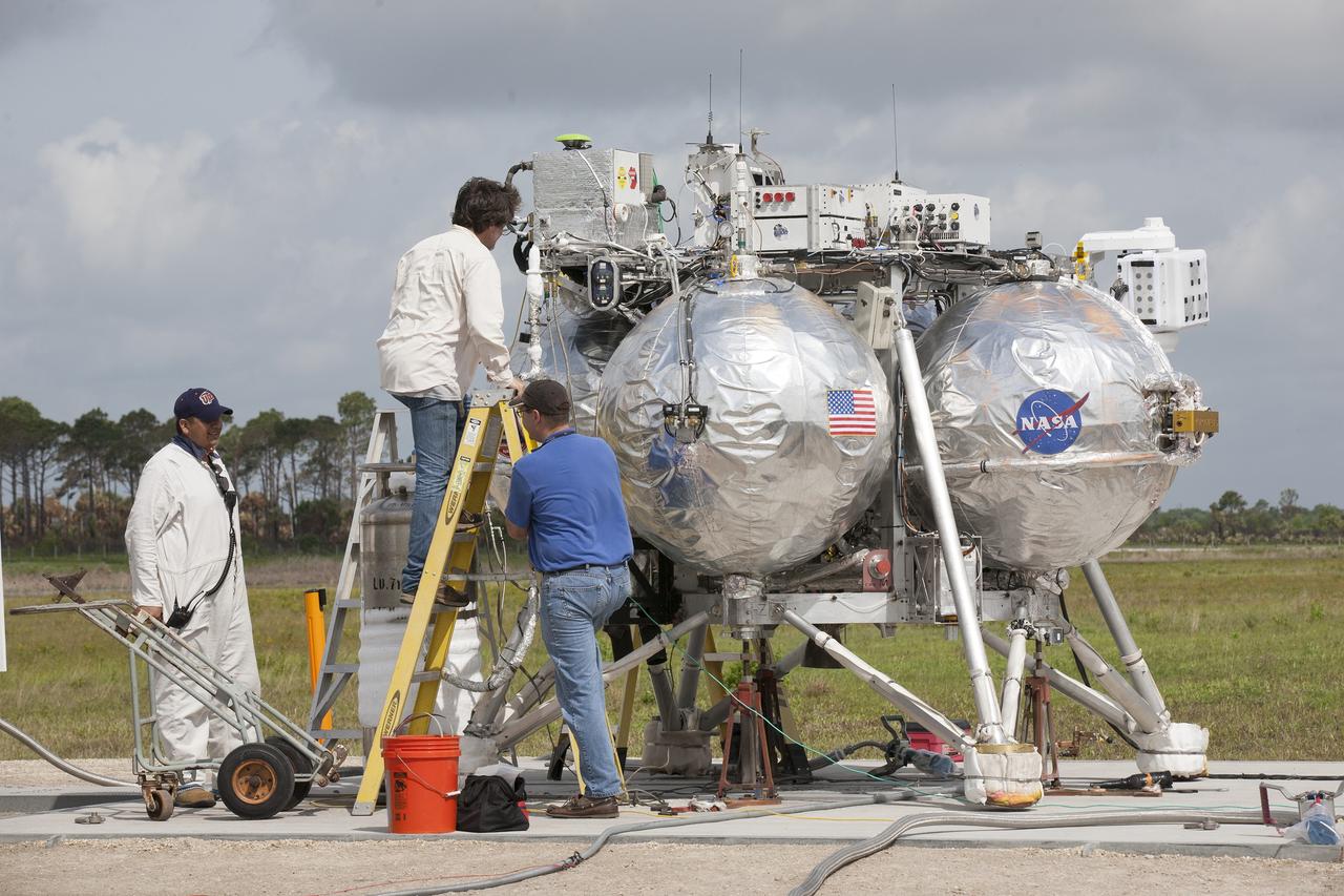 CAPE CANAVERAL, Fla. – Technicians and engineers prepare NASA's Project Morpheus prototype lander for a free-flight test from a new launch pad at the north end of the Shuttle Landing Facility at NASA’s Kennedy Space Center in Florida. The 98-second test began at 1:57 p.m. EDT with the Morpheus lander launching from the ground over a flame trench and ascending more than 800 feet at a peak speed of 36 mph. The vehicle, with its recently installed autonomous landing and hazard avoidance technology, or ALHAT, sensors surveyed the hazard field to determine safe landing sites. Morpheus then flew forward and downward covering approximately 1300 feet while performing a 78-foot divert to simulate a hazard avoidance maneuver. The lander descended and landed on a dedicated pad inside the ALHAT hazard field. Project Morpheus tests NASA’s ALHAT and an engine that runs on liquid oxygen and methane, which are green propellants. These new capabilities could be used in future efforts to deliver cargo to planetary surfaces. The landing facility provides the lander with the kind of field necessary for realistic testing, complete with rocks, craters and hazards to avoid. Morpheus’ ALHAT payload allows it to navigate to clear landing sites amidst rocks, craters and other hazards during its descent. Project Morpheus is being managed under the Advanced Exploration Systems, or AES, Division in NASA’s Human Exploration and Operations Mission Directorate. The efforts in AES pioneer new approaches for rapidly developing prototype systems, demonstrating key capabilities and validating operational concepts for future human missions beyond Earth orbit. For more information on Project Morpheus, visit http://morpheuslander.jsc.nasa.gov/. Photo credit: NASA/Kim Shiflett