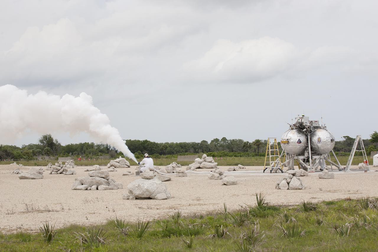 CAPE CANAVERAL, Fla. – A technician vents off the gas from the propellant lines of NASA's Project Morpheus prototype lander after it completed a free-flight test at the north end of the Shuttle Landing Facility at NASA's Kennedy Space Center in Florida. The 98-second test began at 1:57 p.m. EDT with the Morpheus lander launching from the ground over a flame trench and ascending more than 800 feet at a peak speed of 36 mph. The vehicle, with its recently installed autonomous landing and hazard avoidance technology, or ALHAT, sensors surveyed the hazard field to determine safe landing sites. Morpheus then flew forward and downward covering approximately 1300 feet while performing a 78-foot divert to simulate a hazard avoidance maneuver. The lander descended and landed on a dedicated pad inside the ALHAT hazard field. Project Morpheus tests NASA’s ALHAT and an engine that runs on liquid oxygen and methane, which are green propellants. These new capabilities could be used in future efforts to deliver cargo to planetary surfaces.    The landing facility provides the lander with the kind of field necessary for realistic testing, complete with rocks, craters and hazards to avoid. Morpheus’ ALHAT payload allows it to navigate to clear landing sites amidst rocks, craters and other hazards during its descent. Project Morpheus is being managed under the Advanced Exploration Systems, or AES, Division in NASA’s Human Exploration and Operations Mission Directorate. The efforts in AES pioneer new approaches for rapidly developing prototype systems, demonstrating key capabilities and validating operational concepts for future human missions beyond Earth orbit. For more information on Project Morpheus, visit http://morpheuslander.jsc.nasa.gov/.  Photo credit: NASA/Kim Shiflett
