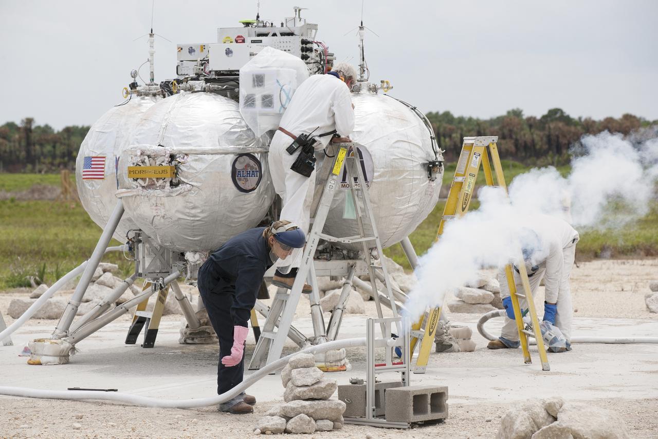 CAPE CANAVERAL, Fla. – Technicians vent off the gas from the propellant lines of NASA's Project Morpheus prototype lander after it completed a free-flight test at the north end of the Shuttle Landing Facility at NASA's Kennedy Space Center in Florida. The 98-second test began at 1:57 p.m. EDT with the Morpheus lander launching from the ground over a flame trench and ascending more than 800 feet at a peak speed of 36 mph. The vehicle, with its recently installed autonomous landing and hazard avoidance technology, or ALHAT, sensors surveyed the hazard field to determine safe landing sites. Morpheus then flew forward and downward covering approximately 1300 feet while performing a 78-foot divert to simulate a hazard avoidance maneuver. The lander descended and landed on a dedicated pad inside the ALHAT hazard field. Project Morpheus tests NASA’s ALHAT and an engine that runs on liquid oxygen and methane, which are green propellants. These new capabilities could be used in future efforts to deliver cargo to planetary surfaces.    The landing facility provides the lander with the kind of field necessary for realistic testing, complete with rocks, craters and hazards to avoid. Morpheus’ ALHAT payload allows it to navigate to clear landing sites amidst rocks, craters and other hazards during its descent. Project Morpheus is being managed under the Advanced Exploration Systems, or AES, Division in NASA’s Human Exploration and Operations Mission Directorate. The efforts in AES pioneer new approaches for rapidly developing prototype systems, demonstrating key capabilities and validating operational concepts for future human missions beyond Earth orbit. For more information on Project Morpheus, visit http://morpheuslander.jsc.nasa.gov/.  Photo credit: NASA/Kim Shiflett