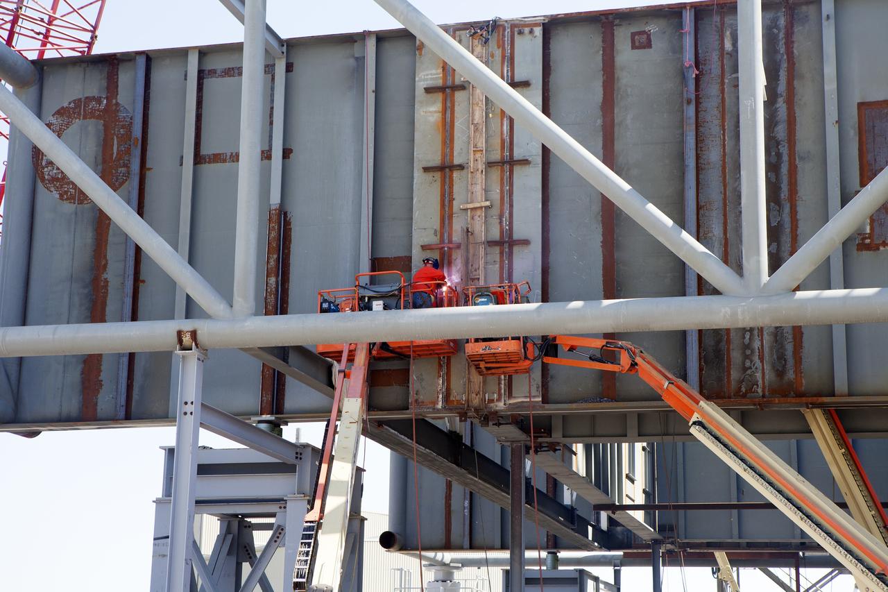 CAPE CANAVERAL, Fla. – Modifications continue on the Mobile Launcher, or ML, at the Mobile Launcher Park Site at NASA’s Kennedy Space Center in Florida. Construction workers on lifts are welding sections of the steel walls. The ML is being modified and strengthened to accommodate the weight, size and thrust at launch of NASA's Space Launch System, or SLS, and Orion spacecraft.    In 2013, the agency awarded a contract to J.P. Donovan Construction Inc. of Rockledge, Fla., to modify the ML, which is one of the key elements of ground support equipment that is being upgraded by the Ground Systems Development and Operations Program office at Kennedy. The existing 24-foot exhaust hole is being enlarged and strengthened for the larger, heavier SLS rocket. The ML will carry the SLS rocket and Orion spacecraft to Launch Pad 39B for its first mission, Exploration Mission-1, in 2017. Photo credit: NASA/Daniel Casper