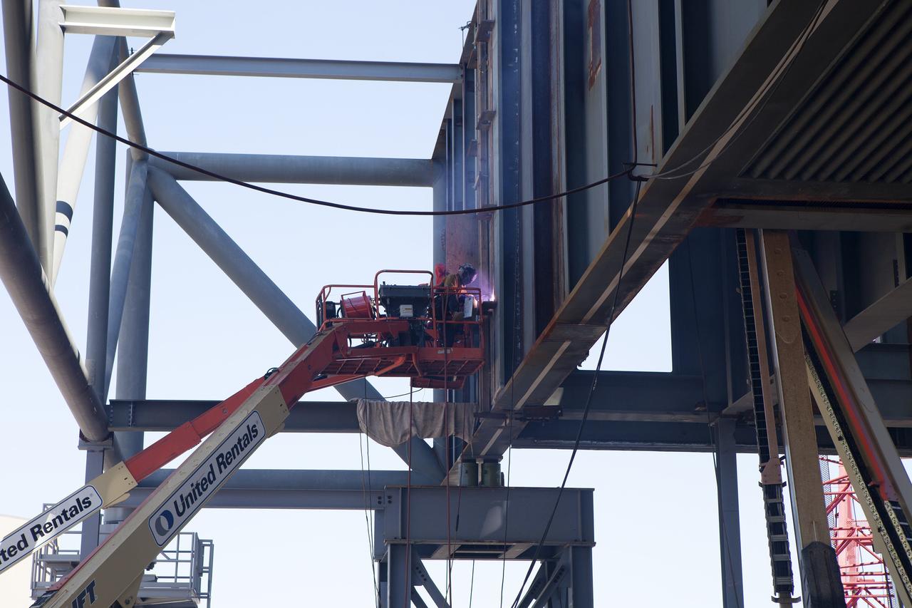 CAPE CANAVERAL, Fla. – Modifications continue on the Mobile Launcher, or ML, at the Mobile Launcher Park Site at NASA’s Kennedy Space Center in Florida. Construction workers on lifts are welding sections of the steel walls. The ML is being modified and strengthened to accommodate the weight, size and thrust at launch of NASA's Space Launch System, or SLS, and Orion spacecraft.    In 2013, the agency awarded a contract to J.P. Donovan Construction Inc. of Rockledge, Fla., to modify the ML, which is one of the key elements of ground support equipment that is being upgraded by the Ground Systems Development and Operations Program office at Kennedy. The existing 24-foot exhaust hole is being enlarged and strengthened for the larger, heavier SLS rocket. The ML will carry the SLS rocket and Orion spacecraft to Launch Pad 39B for its first mission, Exploration Mission-1, in 2017. Photo credit: NASA/Daniel Casper