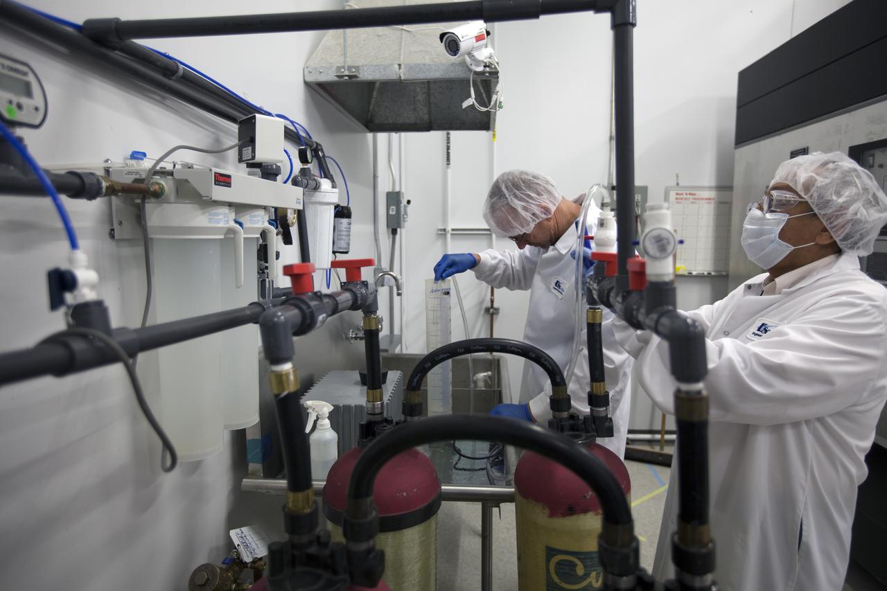 CAPE CANAVERAL, Fla. – Researchers acquire the ionized water for the Veggie plant growth system inside a control chamber at the Space Station Processing Facility at NASA's Kennedy Space Center in Florida. From left, are Jim Smodell, a technician with SGT, and George Guerra, a quality control engineer with QinetiQ North America. The growth chamber will be used as a control unit and procedures will be followed identical to those being performed on Veggie and the Veg-01 experiment on the International Space Station by Expedition 39 flight engineer and NASA astronaut Steve Swanson.    Veggie and Veg-01 were delivered to the space station aboard the SpaceX-3 mission. Veggie is the first fresh food production system delivered to the station. Six plant pillows, each containing outredgeous red romaine lettuce seeds and a root mat were inserted into Veggie. The plant chamber's red, blue and green LED lights were activated. The plant growth will be monitored for 28 days. At the end of the cycle, the plants will be carefully harvested, frozen and stored for return to Earth. Photo credit: NASA/Dimitri Gerondidakis