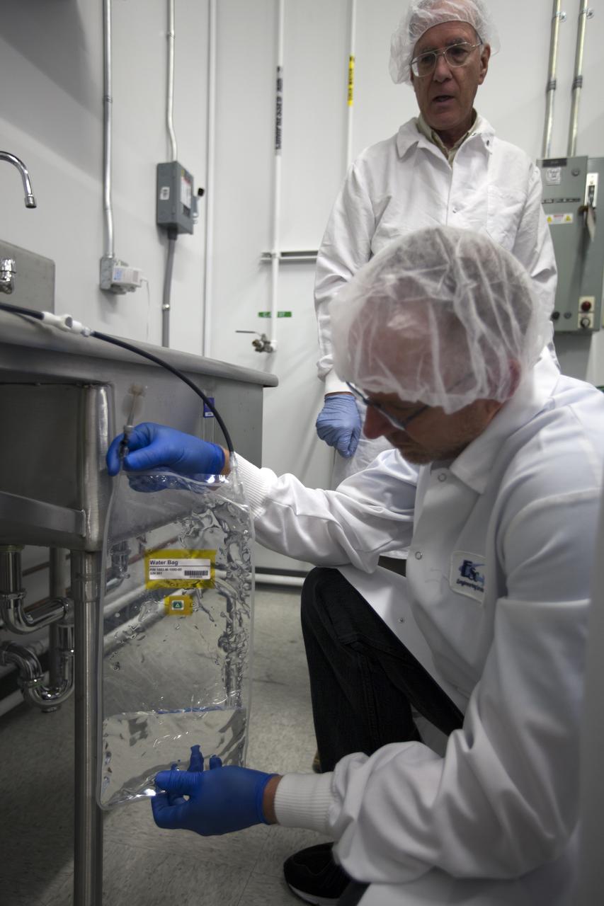 CAPE CANAVERAL, Fla. – Researchers fill a water bag with ionized water for the Veggie plant growth system inside a control chamber at the Space Station Processing Facility at NASA's Kennedy Space Center in Florida. In front is Jim Smodell, a technician with SGT. Standing behind him is Chuck Spern, lead project engineer with QinetiQ North America. The growth chamber will be used as a control unit and procedures will be followed identical to those being performed on Veggie and the Veg-01 experiment on the International Space Station by Expedition 39 flight engineer and NASA astronaut Steve Swanson.    Veggie and Veg-01 were delivered to the space station aboard the SpaceX-3 mission. Veggie is the first fresh food production system delivered to the station. Six plant pillows, each containing outredgeous red romaine lettuce seeds and a root mat were inserted into Veggie. The plant chamber's red, blue and green LED lights were activated. The plant growth will be monitored for 28 days. At the end of the cycle, the plants will be carefully harvested, frozen and stored for return to Earth. Photo credit: NASA/Dimitri Gerondidakis