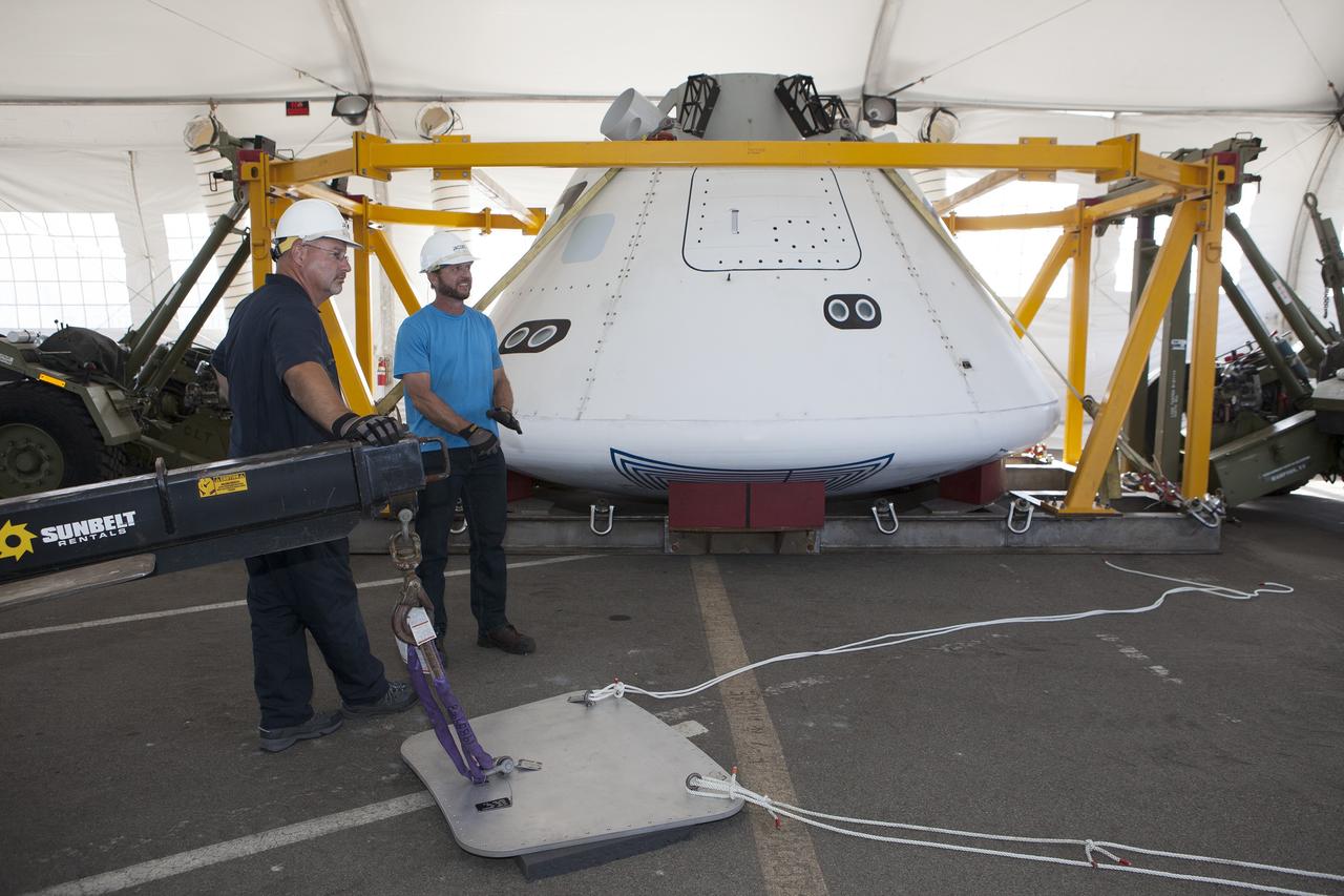 SAN DIEGO, Calif. – Inside a protective structure at the Mole Pier at the Naval Base San Diego in California, workers prepare for a simulated fit check of the hatch cover on the Orion boilerplate test vehicle. The test vehicle is secured on the crew module recovery cradle. The Ground Systems Development and Operations Program, Lockheed Martin and the U.S. Navy are evaluating the hardware and processes for preparing the Orion crew module for Exploration Flight Test-1, or EFT-1, for overland transport from the naval base to NASA's Kennedy Space Center in Florida.    Orion is the exploration spacecraft designed to carry astronauts to destinations not yet explored by humans, including an asteroid and Mars. It will have emergency abort capability, sustain the crew during space travel and provide safe re-entry from deep space return velocities. The first unpiloted test flight of the Orion is scheduled to launch later this year atop a Delta IV rocket from Cape Canaveral Air Force Station in Florida to an altitude of 3,600 miles above the Earth's surface. The two-orbit, four-hour flight test will help engineers evaluate the systems critical to crew safety including the heat shield, parachute system and launch abort system. For more information, visit http://www.nasa.gov/orion. Photo credit: NASA/Kim Shiflett