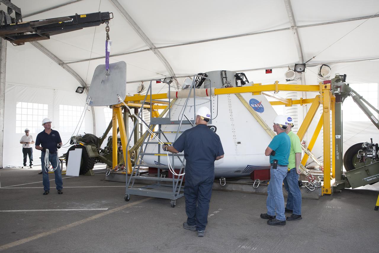 SAN DIEGO, Calif. – Inside a protective structure at the Mole Pier at the Naval Base San Diego in California, workers prepare for a simulated fit check of the hatch cover on the Orion boilerplate test vehicle. The test vehicle is secured on the crew module recovery cradle. The Ground Systems Development and Operations Program, Lockheed Martin and the U.S. Navy are evaluating the hardware and processes for preparing the Orion crew module for Exploration Flight Test-1, or EFT-1, for overland transport from the naval base to NASA's Kennedy Space Center in Florida.    Orion is the exploration spacecraft designed to carry astronauts to destinations not yet explored by humans, including an asteroid and Mars. It will have emergency abort capability, sustain the crew during space travel and provide safe re-entry from deep space return velocities. The first unpiloted test flight of the Orion is scheduled to launch later this year atop a Delta IV rocket from Cape Canaveral Air Force Station in Florida to an altitude of 3,600 miles above the Earth's surface. The two-orbit, four-hour flight test will help engineers evaluate the systems critical to crew safety including the heat shield, parachute system and launch abort system. For more information, visit http://www.nasa.gov/orion. Photo credit: NASA/Kim Shiflett