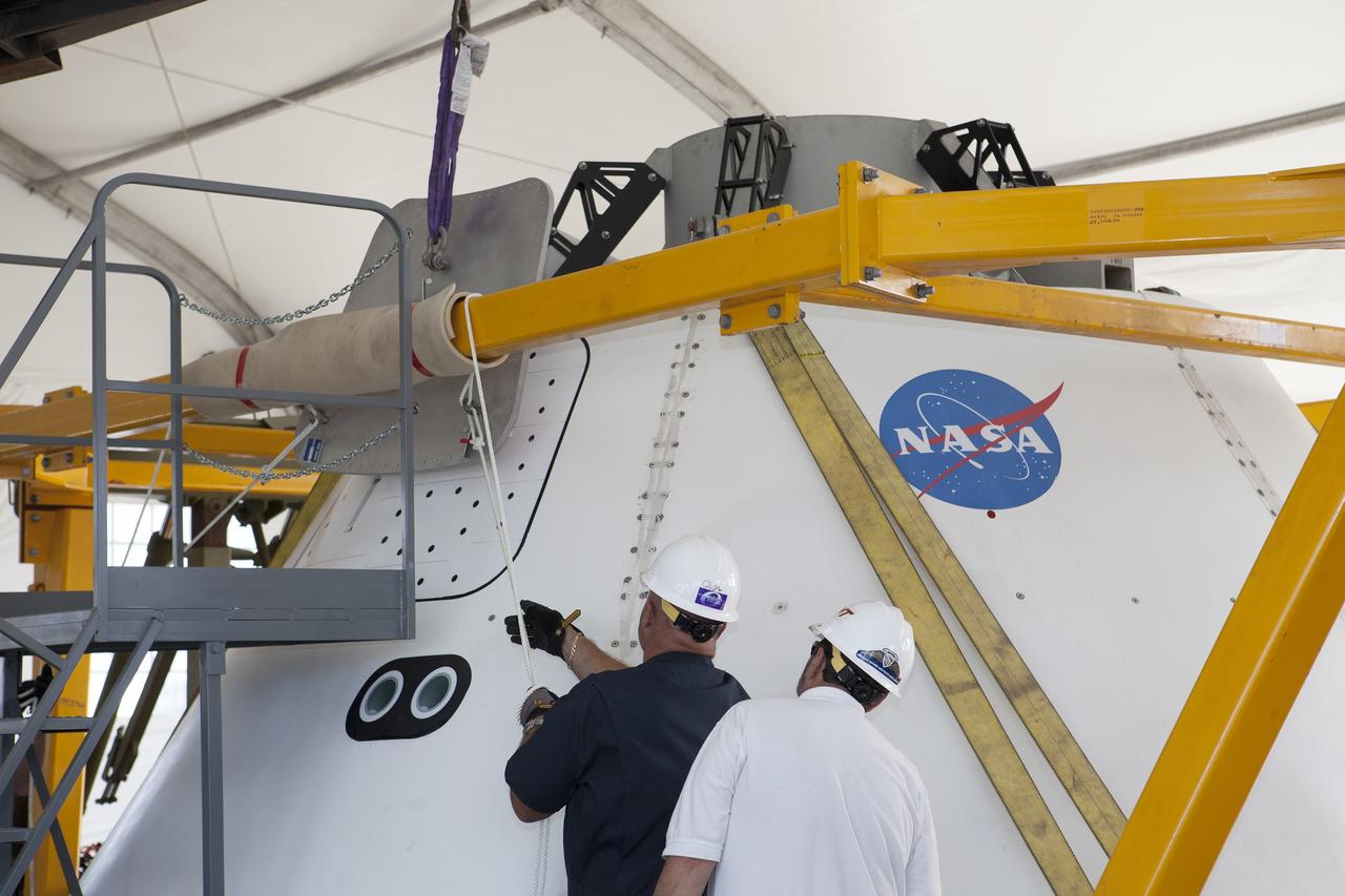 SAN DIEGO, Calif. – Inside a protective structure at the Mole Pier at the Naval Base San Diego in California, workers prepare for a simulated fit check of the hatch cover on the Orion boilerplate test vehicle. The test vehicle is secured on the crew module recovery cradle. The Ground Systems Development and Operations Program, Lockheed Martin and the U.S. Navy are evaluating the hardware and processes for preparing the Orion crew module for Exploration Flight Test-1, or EFT-1, for overland transport from the naval base to NASA's Kennedy Space Center in Florida.    Orion is the exploration spacecraft designed to carry astronauts to destinations not yet explored by humans, including an asteroid and Mars. It will have emergency abort capability, sustain the crew during space travel and provide safe re-entry from deep space return velocities. The first unpiloted test flight of the Orion is scheduled to launch later this year atop a Delta IV rocket from Cape Canaveral Air Force Station in Florida to an altitude of 3,600 miles above the Earth's surface. The two-orbit, four-hour flight test will help engineers evaluate the systems critical to crew safety including the heat shield, parachute system and launch abort system. For more information, visit http://www.nasa.gov/orion. Photo credit: NASA/Kim Shiflett