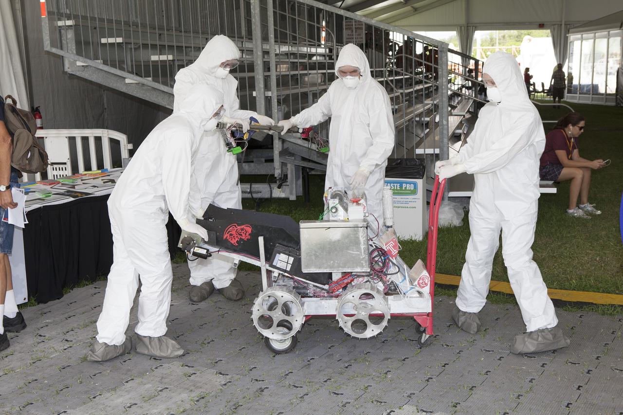 CAPE CANAVERAL, Fla. – College team members, dressed in protective suits, prepare their robot for a trial run at NASA’s Robotics Mining Competition at the Kennedy Space Center Visitor Complex in Florida. More than 35 teams from around the U.S. have designed and built remote-controlled robots for the mining competition. The competition is a NASA Human Exploration and Operations Mission Directorate project designed to engage and retain students in science, technology, engineering and mathematics, or STEM, fields by expanding opportunities for student research and design. Teams use their remote-controlled robotics to maneuver and dig in a supersized sandbox filled with a crushed material that has characteristics similar to Martian soil. The objective of the challenge is to see which team’s robot can collect and move the most regolith within a specified amount of time. For more information, visit www.nasa.gov/nasarmc. Photo credit: NASA/Ben Smegelsky