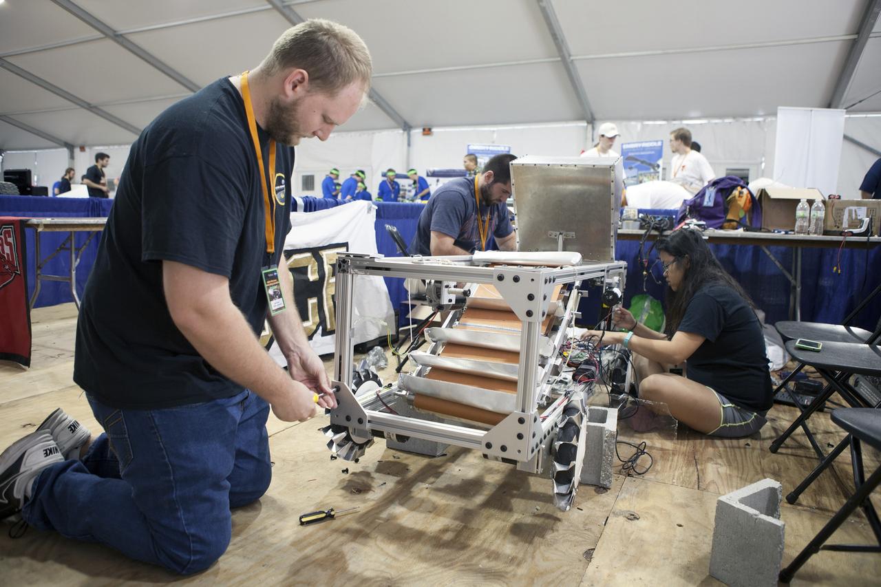 CAPE CANAVERAL, Fla. – The Hawai'l Marsbot Team members from Kapi'olani Community College in Hawaii prepare their robot for the mining portion of NASA's 2014 Robotics Mining Competition at the Kennedy Space Center Visitor Complex in Florida. More than 35 teams from around the U.S. have designed and built remote-controlled robots for the mining competition.    The competition is a NASA Human Exploration and Operations Mission Directorate project designed to engage and retain students in science, technology, engineering and mathematics, or STEM, fields by expanding opportunities for student research and design. Teams use their remote-controlled robotics to maneuver and dig in a supersized sandbox filled with a crushed material that has characteristics similar to Martian soil. The objective of the challenge is to see which team’s robot can collect and move the most regolith within a specified amount of time. For more information, visit www.nasa.gov/nasarmc. Photo credit: NASA/Frankie Martin