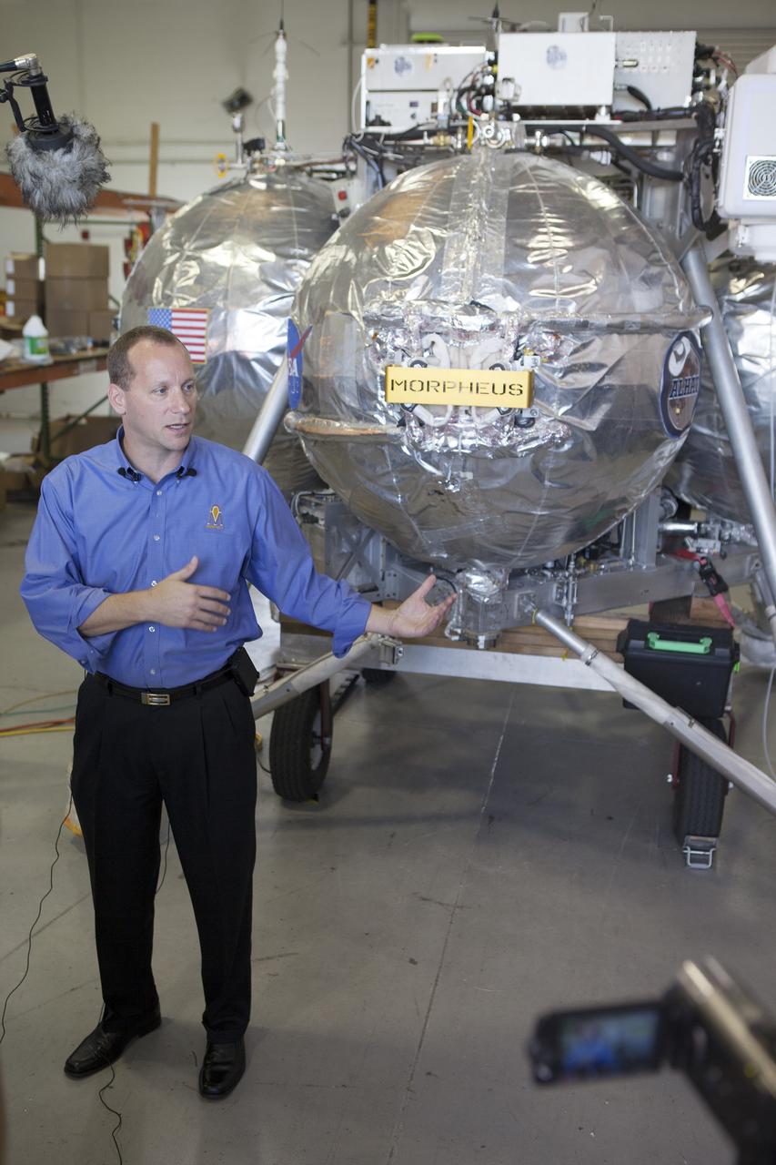 CAPE CANAVERAL, Fla. – Jon Olansen, Morpheus project manager, speaks to members of the media inside a facility near the Shuttle Landing Facility at NASA's Kennedy Space Center in Florida. Behind Olansen is the Project Morpheus prototype lander. Project Morpheus tests NASA’s autonomous landing and hazard avoidance technology, or ALHAT, sensors and an engine that runs on liquid oxygen and methane, which are green propellants. These new capabilities could be used in future efforts to deliver cargo to planetary surfaces.    The landing facility provides the lander with the kind of field necessary for realistic testing, complete with rocks, craters and hazards to avoid. Morpheus’ ALHAT payload allows it to navigate to clear landing sites amidst rocks, craters and other hazards during its descent. Project Morpheus is being managed under the Advanced Exploration Systems, or AES, Division in NASA’s Human Exploration and Operations Mission Directorate. The efforts in AES pioneer new approaches for rapidly developing prototype systems, demonstrating key capabilities and validating operational concepts for future human missions beyond Earth orbit. For more information on Project Morpheus, visit http://morpheuslander.jsc.nasa.gov/.  Photo credit: NASA/Frankie Martin