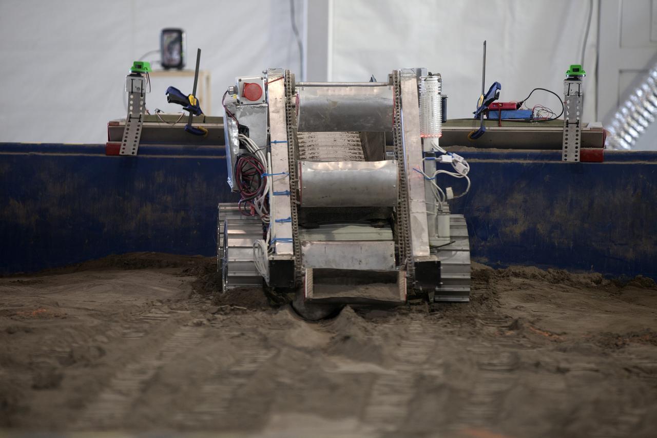 CAPE CANAVERAL, Fla. – A robot digs in the simulated Martian soil in the Caterpillar Mining Arena during NASA’s 2014 Robotic Mining Competition at the Kennedy Space Center Visitor Complex in Florida. More than 35 teams from around the U.S. have designed and built remote-controlled robots for the mining competition. The competition is a NASA Human Exploration and Operations Mission Directorate project designed to engage and retain students in science, technology, engineering and mathematics, or STEM, fields by expanding opportunities for student research and design. Teams use their remote-controlled robotics to maneuver and dig in a supersized sandbox filled with a crushed material that has characteristics similar to Martian soil. The objective of the challenge is to see which team’s robot can collect and move the most regolith within a specified amount of time. For more information, visit www.nasa.gov/nasarmc. Photo credit: NASA/Kim Shiflett