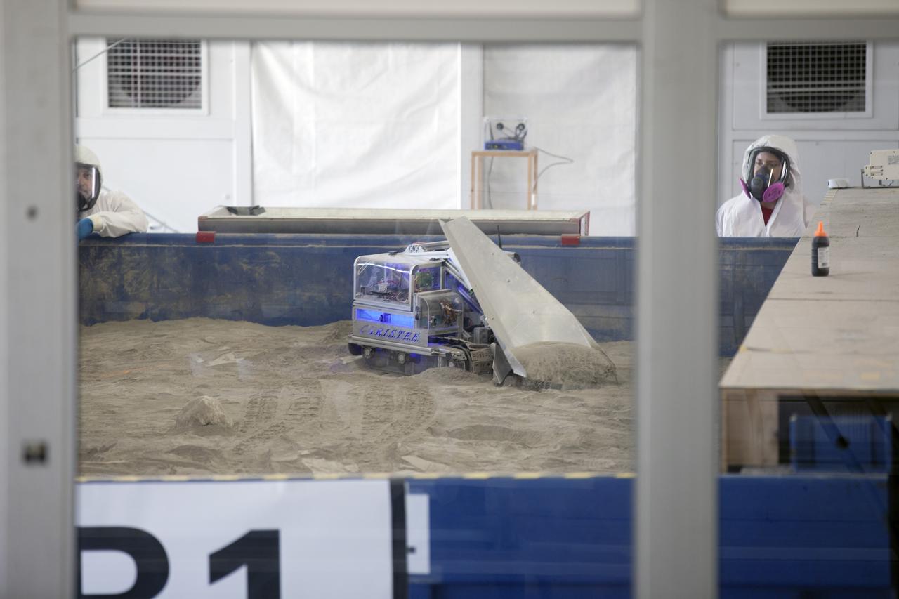 CAPE CANAVERAL, Fla. – A robot digs in the simulated Martian soil in the Caterpillar Mining Arena during NASA’s 2014 Robotic Mining Competition at the Kennedy Space Center Visitor Complex in Florida. More than 35 teams from colleges and universities around the U.S. have designed and built remote-controlled robots for the mining competition. The competition is a NASA Human Exploration and Operations Mission Directorate project designed to engage and retain students in science, technology, engineering and mathematics, or STEM, fields by expanding opportunities for student research and design. Teams use their remote-controlled robotics to maneuver and dig in a supersized sandbox filled with a crushed material that has characteristics similar to Martian soil. The objective of the challenge is to see which team’s robot can collect and move the most regolith within a specified amount of time. For more information, visit www.nasa.gov/nasarmc. Photo credit: NASA/Kim Shiflett