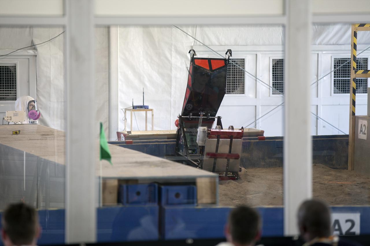 CAPE CANAVERAL, Fla. – A robot dumps its load of simulated Martian soil in a collector in the Caterpillar Mining Arena during NASA’s 2014 Robotic Mining Competition at the Kennedy Space Center Visitor Complex in Florida. A competition judge monitors the progress. More than 35 teams from colleges and universities around the U.S. have designed and built remote-controlled robots for the mining competition. The competition is a NASA Human Exploration and Operations Mission Directorate project designed to engage and retain students in science, technology, engineering and mathematics, or STEM, fields by expanding opportunities for student research and design. Teams use their remote-controlled robotics to maneuver and dig in a supersized sandbox filled with a crushed material that has characteristics similar to Martian soil. The objective of the challenge is to see which team’s robot can collect and move the most regolith within a specified amount of time. For more information, visit www.nasa.gov/nasarmc. Photo credit: NASA/Kim Shiflett