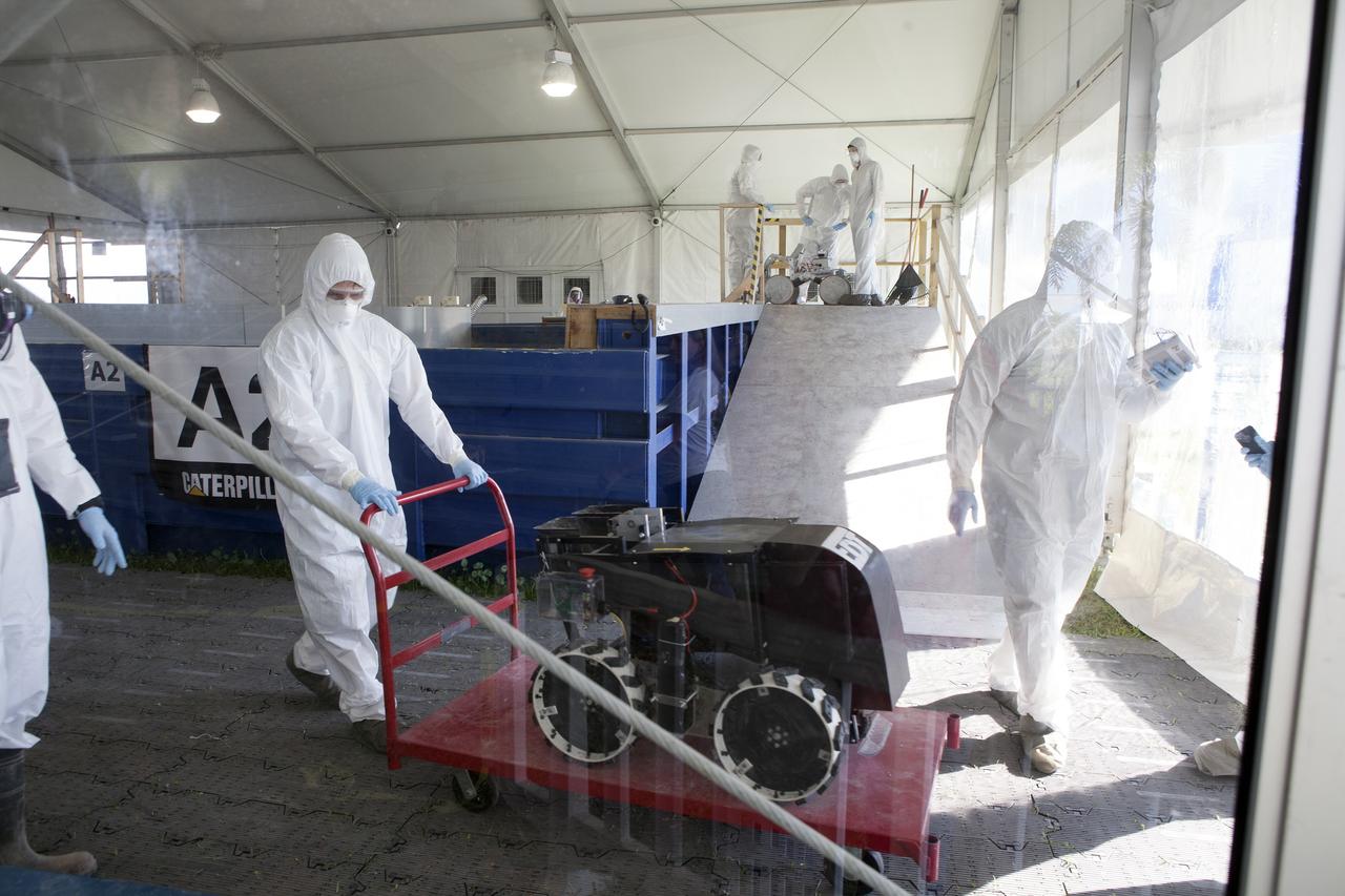 CAPE CANAVERAL, Fla. – A mining team exits the Caterpillar Mining Area with its robot as another team prepares to lower its robot into the simulated Martian soil during NASA’s 2014 Robotic Mining Competition at the Kennedy Space Center Visitor Complex in Florida. More than 35 teams from colleges and universities around the U.S. have designed and built remote-controlled robots for the mining competition. The competition is a NASA Human Exploration and Operations Mission Directorate project designed to engage and retain students in science, technology, engineering and mathematics, or STEM, fields by expanding opportunities for student research and design. Teams use their remote-controlled robotics to maneuver and dig in a supersized sandbox filled with a crushed material that has characteristics similar to Martian soil. The objective of the challenge is to see which team’s robot can collect and move the most regolith within a specified amount of time. For more information, visit www.nasa.gov/nasarmc. Photo credit: NASA/Kim Shiflett