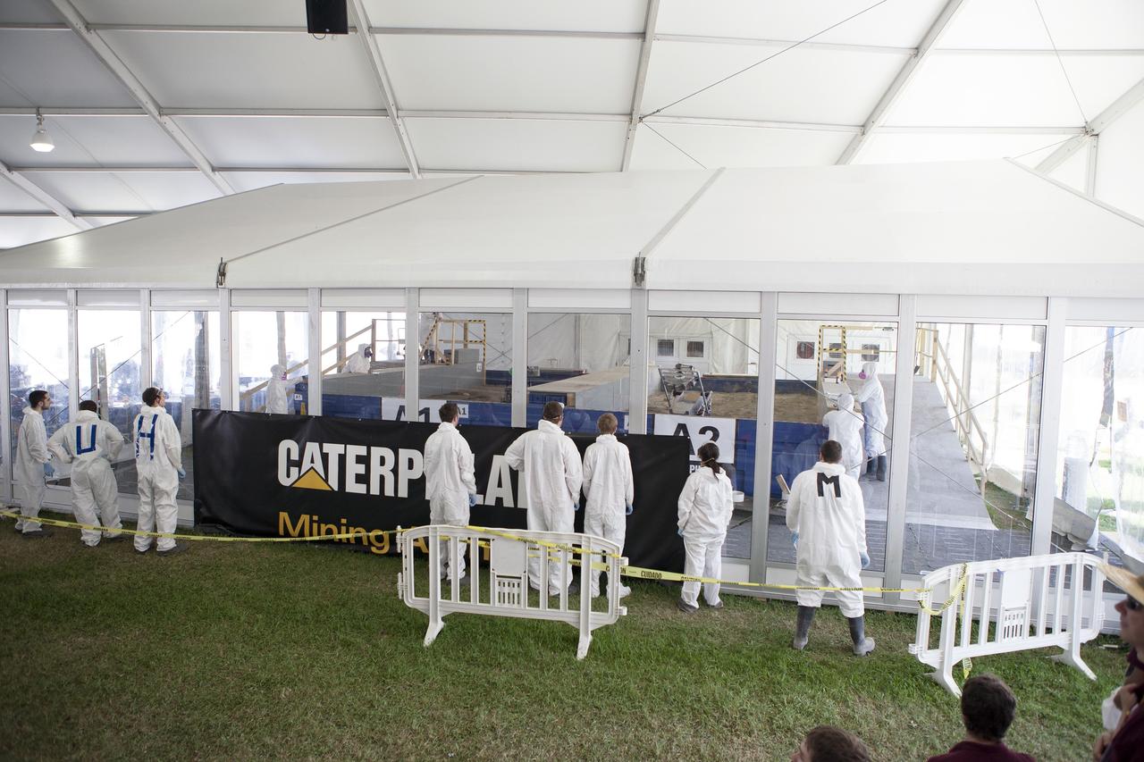 CAPE CANAVERAL, Fla. – Team members watch their robots dig in the simulated Martian soil in the Caterpillar Mining Arena during NASA’s 2014 Robotic Mining Competition at the Kennedy Space Center Visitor Complex in Florida. Competition judge monitor the progress inside the arena. More than 35 teams from colleges and universities around the U.S. have designed and built remote-controlled robots for the mining competition. The competition is a NASA Human Exploration and Operations Mission Directorate project designed to engage and retain students in science, technology, engineering and mathematics, or STEM, fields by expanding opportunities for student research and design. Teams use their remote-controlled robotics to maneuver and dig in a supersized sandbox filled with a crushed material that has characteristics similar to Martian soil. The objective of the challenge is to see which team’s robot can collect and move the most regolith within a specified amount of time. For more information, visit www.nasa.gov/nasarmc. Photo credit: NASA/Kim Shiflett