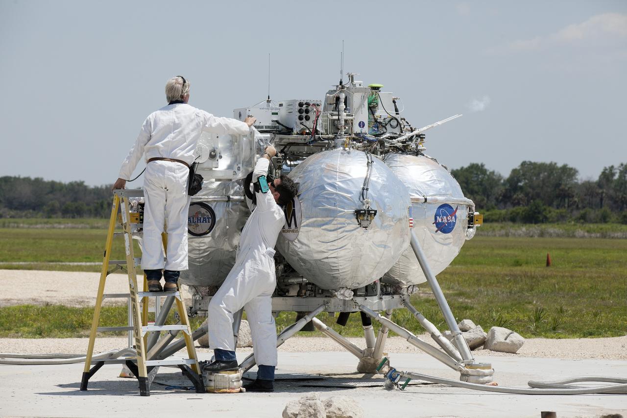 CAPE CANAVERAL, Fla. – At NASA's Kennedy Space Center in Florida, technicians check out the agency's Project Morpheus prototype lander which just touched down on a dedicated pad inside the ALHAT hazard field near the Shuttle Landing Facility. Project Morpheus tests NASA’s ALHAT and an engine that runs on liquid oxygen and methane, which are green propellants. These new capabilities could be used in future efforts to deliver cargo to planetary surfaces.      The landing facility provides the lander with the kind of field necessary for realistic testing, complete with rocks, craters and hazards to avoid. Morpheus’ ALHAT payload allows it to navigate to clear landing sites amidst rocks, craters and other hazards during its descent. Project Morpheus is being managed under the Advanced Exploration Systems, or AES, Division in NASA’s Human Exploration and Operations Mission Directorate. The efforts in AES pioneer new approaches for rapidly developing prototype systems, demonstrating key capabilities and validating operational concepts for future human missions beyond Earth orbit. For more information on Project Morpheus, visit http://morpheuslander.jsc.nasa.gov/. Photo credit: NASA/Kim Shiflett