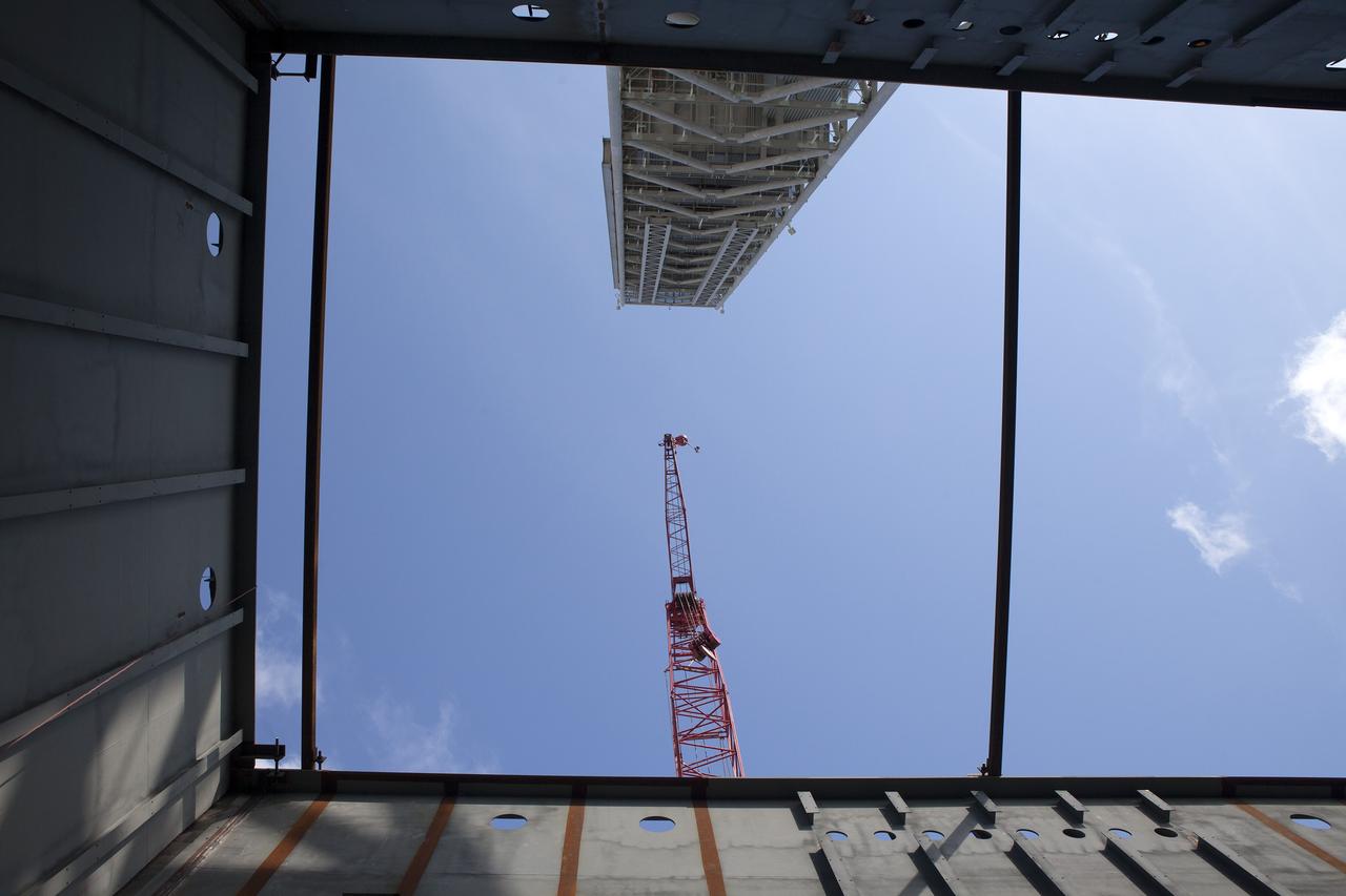 CAPE CANAVERAL, Fla. -- Modifications continue on the Mobile Launcher, or ML, at the Mobile Launcher Park Site at NASA’s Kennedy Space Center in Florida. In this view looking up from beneath the ML, the tower and a large crane are visible. The crane is situated near the ML for lifting of heavy metal beams and other construction materials. Sections of the ML are being modified and strengthened to accommodate the weight, size and thrust at launch of NASA's Space Launch System and Orion spacecraft.    In 2013, the agency awarded a contract to J.P. Donovan Construction Inc. of Rockledge, Fla., to modify the ML, which is one of the key elements of ground support equipment that is being upgraded by the Ground Systems Development and Operations Program office at Kennedy. The existing 24-foot exhaust hole is being enlarged and strengthened for the larger, heavier SLS rocket. The ML will carry the SLS rocket and Orion spacecraft to Launch Pad 39B for its first mission, Exploration Mission-1, in 2017. Photo credit: NASA/Daniel Casper