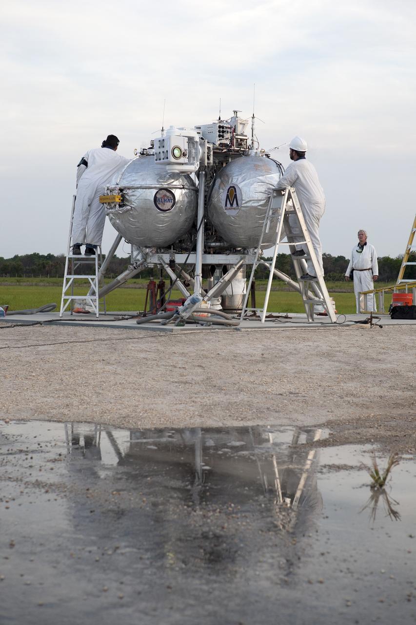 CAPE CANAVERAL, Fla. -- Technicians check the systems on NASA's Project Morpheus prototype lander in preparation for the first free flight test at night from a launch pad at the north end of the Shuttle Landing Facility at NASA's Kennedy Space Center in Florida. The 98-second test began at 10:02 p.m. EDT with the Morpheus lander launching from the ground over a flame trench and ascending more than 800 feet. The vehicle, with its autonomous landing and hazard avoidance technology, or ALHAT sensors, surveyed the hazard field to determine safe landing sites. Morpheus then flew forward and downward covering approximately 1,300 feet while performing a 78-foot divert to simulate a hazard avoidance maneuver. The lander then descended and landed on a dedicated pad inside the test field. Project Morpheus tests NASA’s ALHAT and an engine that runs on liquid oxygen and methane, which are green propellants. These new capabilities could be used in future efforts to deliver cargo to planetary surfaces. The landing facility provides the lander with the kind of field necessary for realistic testing, complete with rocks, craters and hazards to avoid. Morpheus’ ALHAT payload allows it to navigate to clear landing sites amidst rocks, craters and other hazards during its descent. Project Morpheus is being managed under the Advanced Exploration Systems, or AES, Division in NASA’s Human Exploration and Operations Mission Directorate. The efforts in AES pioneer new approaches for rapidly developing prototype systems, demonstrating key capabilities and validating operational concepts for future human missions beyond Earth orbit. For more information on Project Morpheus, visit http://morpheuslander.jsc.nasa.gov/. Photo credit: NASA/Kim Shiflett