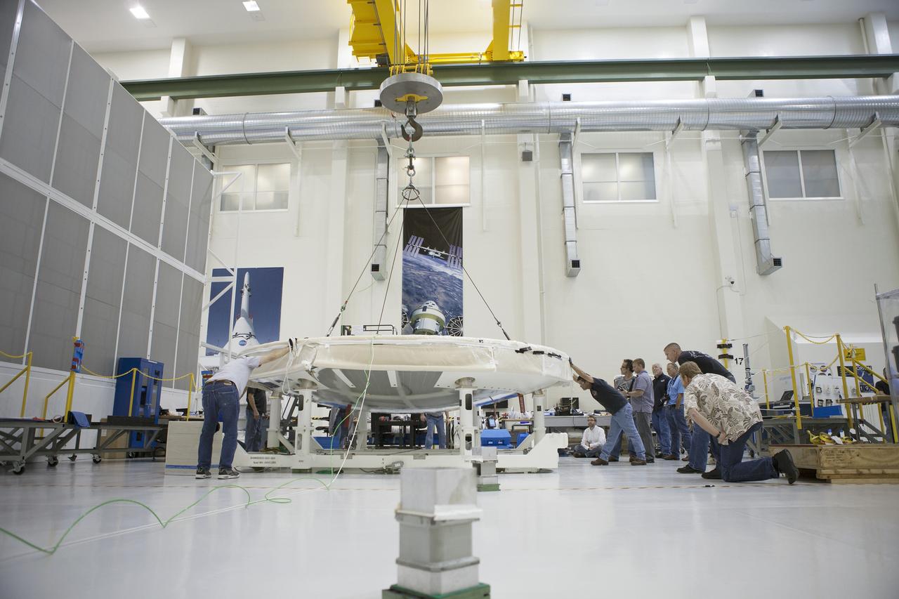 CAPE CANAVERAL, Fla. -- Lockheed Martin technicians and engineers monitor the progress and assist as needed as a crane begins to lift the Orion heat shield away from a stand inside the Operations and Checkout Building high bay at NASA's Kennedy Space Center in Florida. Technicians have installed more than 200 instrumentation sensors on the heat shield and are preparing it for installation on the Orion crew module.    Orion is the exploration spacecraft designed to carry astronauts to destinations not yet explored by humans, including an asteroid and Mars. It will have emergency abort capability, sustain the crew during space travel and provide safe re-entry from deep space return velocities. The first unpiloted test flight of the Orion is scheduled to launch later this year atop a Delta IV rocket from Cape Canaveral Air Force Station in Florida to an altitude of 3,600 miles above the Earth's surface. The two-orbit, four-hour flight test will help engineers evaluate the systems critical to crew safety including the heat shield, parachute system and launch abort system. For more information, visit http://www.nasa.gov/orion. Photo credit: NASA/Frankie Martin