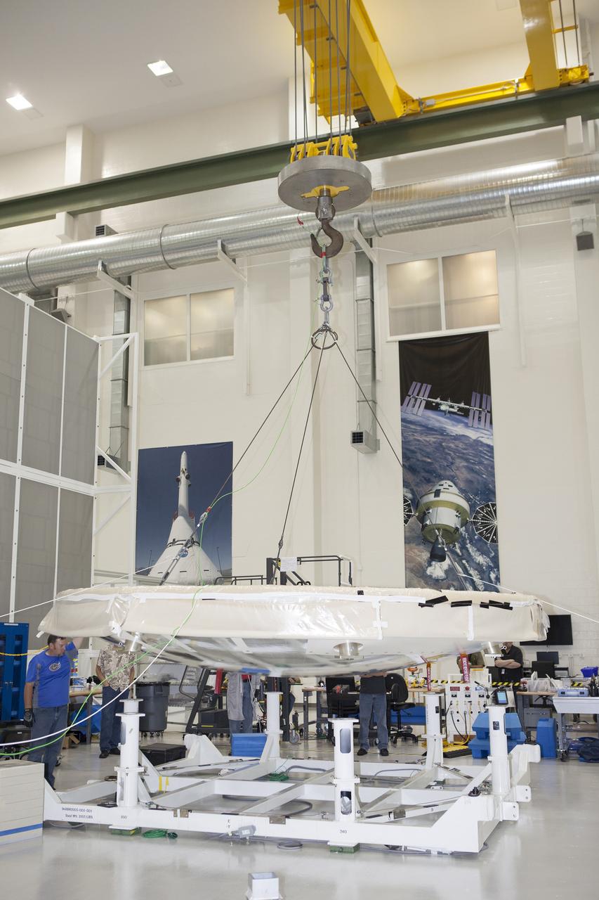CAPE CANAVERAL, Fla. -- Lockheed Martin technicians and engineers monitor the progress as a crane lifts the Orion heat shield away from a stand inside the Operations and Checkout Building high bay at NASA's Kennedy Space Center in Florida. Technicians have installed more than 200 instrumentation sensors on the heat shield and are preparing it for installation on the Orion crew module.    Orion is the exploration spacecraft designed to carry astronauts to destinations not yet explored by humans, including an asteroid and Mars. It will have emergency abort capability, sustain the crew during space travel and provide safe re-entry from deep space return velocities. The first unpiloted test flight of the Orion is scheduled to launch later this year atop a Delta IV rocket from Cape Canaveral Air Force Station in Florida to an altitude of 3,600 miles above the Earth's surface. The two-orbit, four-hour flight test will help engineers evaluate the systems critical to crew safety including the heat shield, parachute system and launch abort system. For more information, visit http://www.nasa.gov/orion. Photo credit: NASA/Frankie Martin