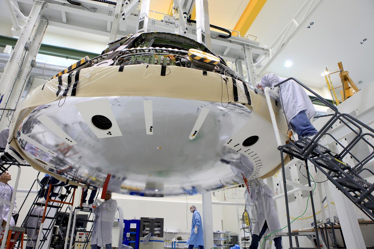 CAPE CANAVERAL, Fla. -- Lockheed Martin technicians and engineers attach the heat shield to the Orion crew module inside the Operations and Checkout Building high bay at NASA's Kennedy Space Center in Florida. Technicians have installed more than 200 instrumentation sensors on the heat shield for Exploration Flight Test-1, or EFT-1. The flight test will provide engineers with data about the heat shield's ability to protect Orion and its future crews from the 4,000-degree heat of reentry and an ocean splashdown following the spacecraft’s 20,000-mph reentry from space. Data gathered during the flight will inform decisions about design improvements on the heat shield and other Orion systems, and authenticate existing computer models and new approaches to space systems design and development. This process is critical to reducing overall risks and costs of future Orion missions.    Orion is the exploration spacecraft designed to carry astronauts to destinations not yet explored by humans, including an asteroid and Mars. It will have emergency abort capability, sustain the crew during space travel and provide safe re-entry from deep space return velocities. The first unpiloted test flight of the Orion is scheduled to launch later this year atop a Delta IV rocket from Cape Canaveral Air Force Station in Florida to an altitude of 3,600 miles above the Earth's surface. The two-orbit, four-hour flight test will help engineers evaluate the systems critical to crew safety including the heat shield, parachute system and launch abort system. For more information, visit http://www.nasa.gov/orion. Photo credit: NASA/Daniel Casper
